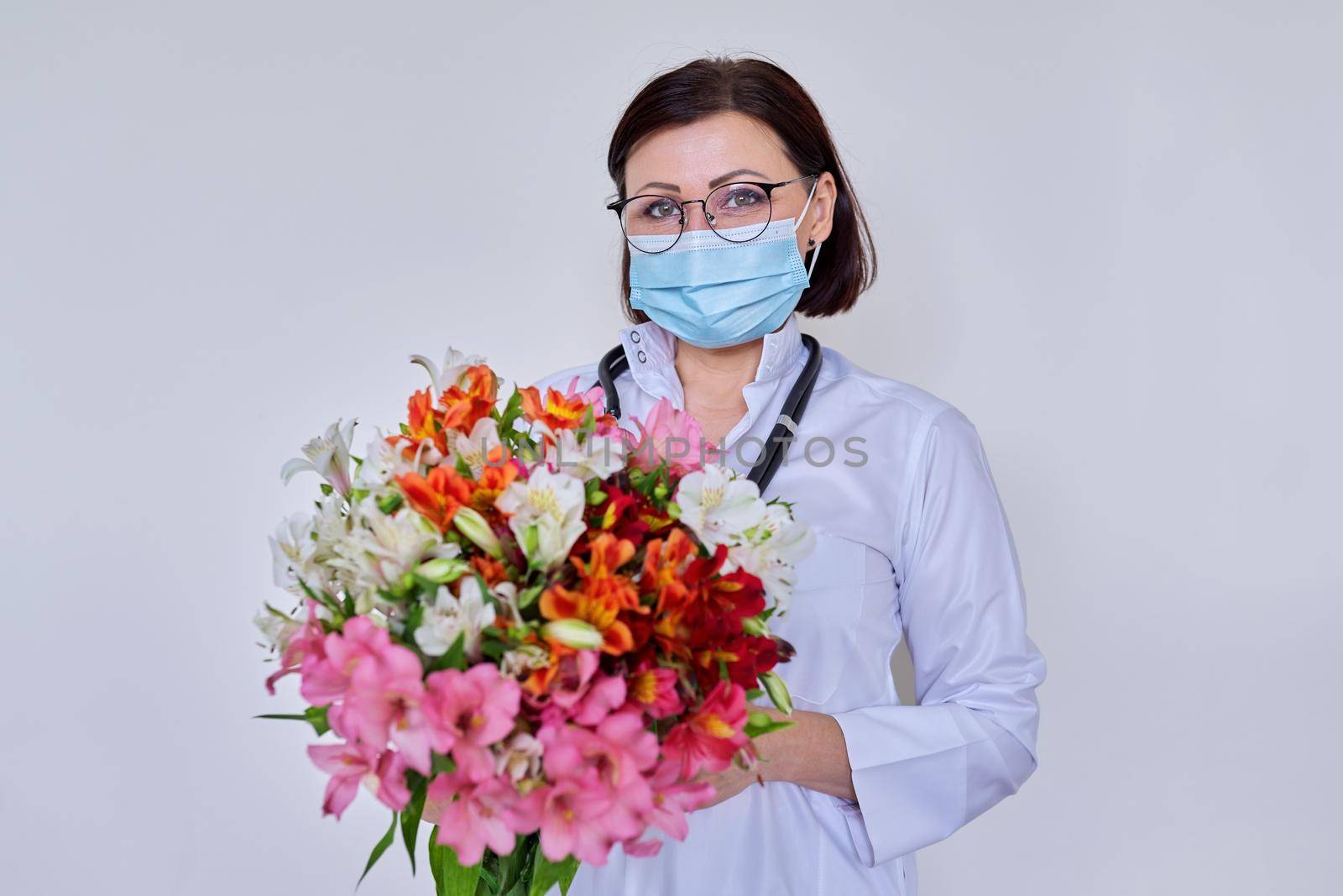 Female doctor in a medical protective mask on her face and a bouquet of flowers by VH-studio