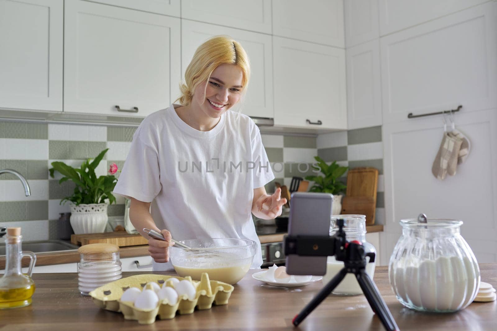 Female teenager learns to cook pancakes, watching video recipe on smartphone by VH-studio