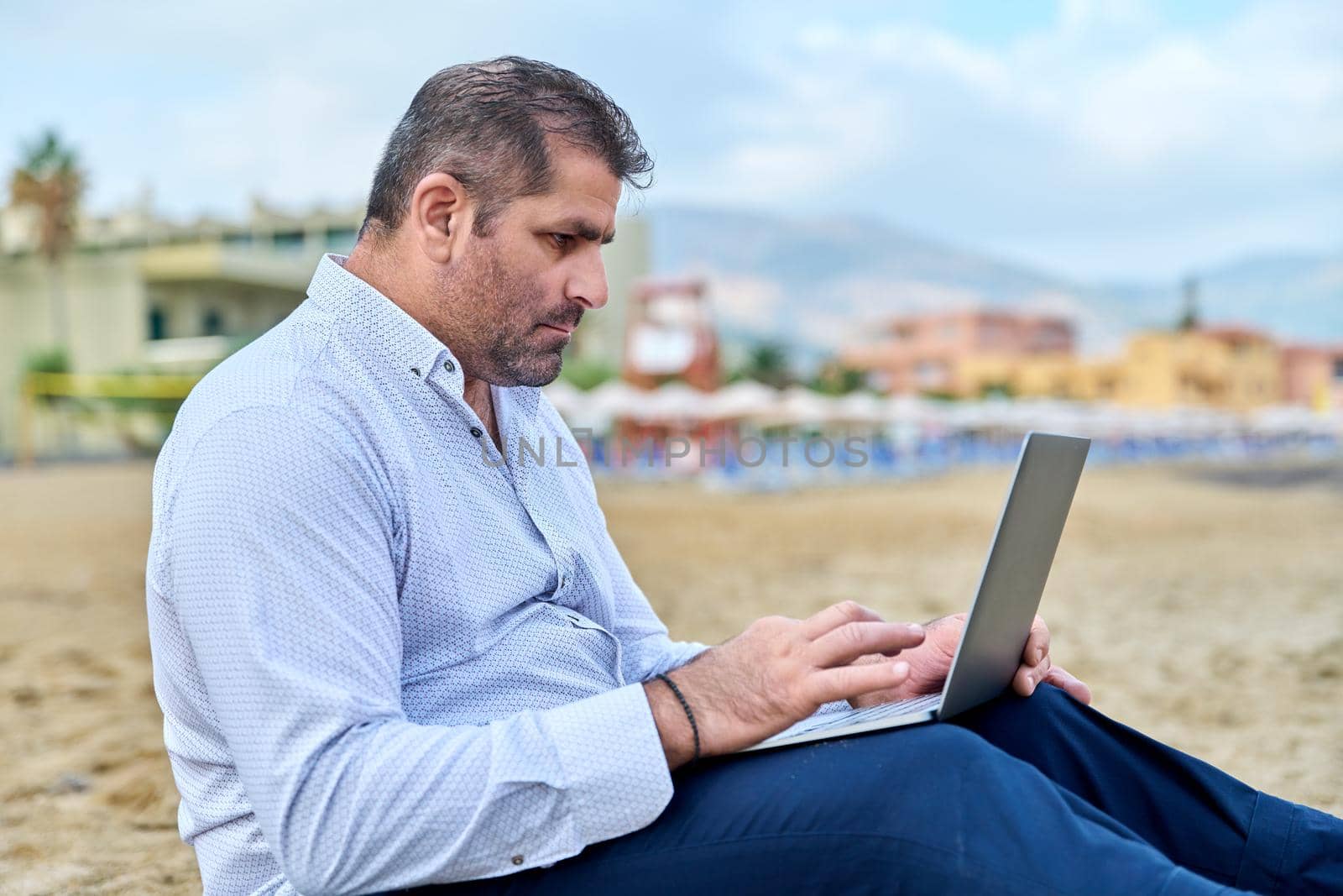 Serious confident mature man with laptop outdoors by VH-studio