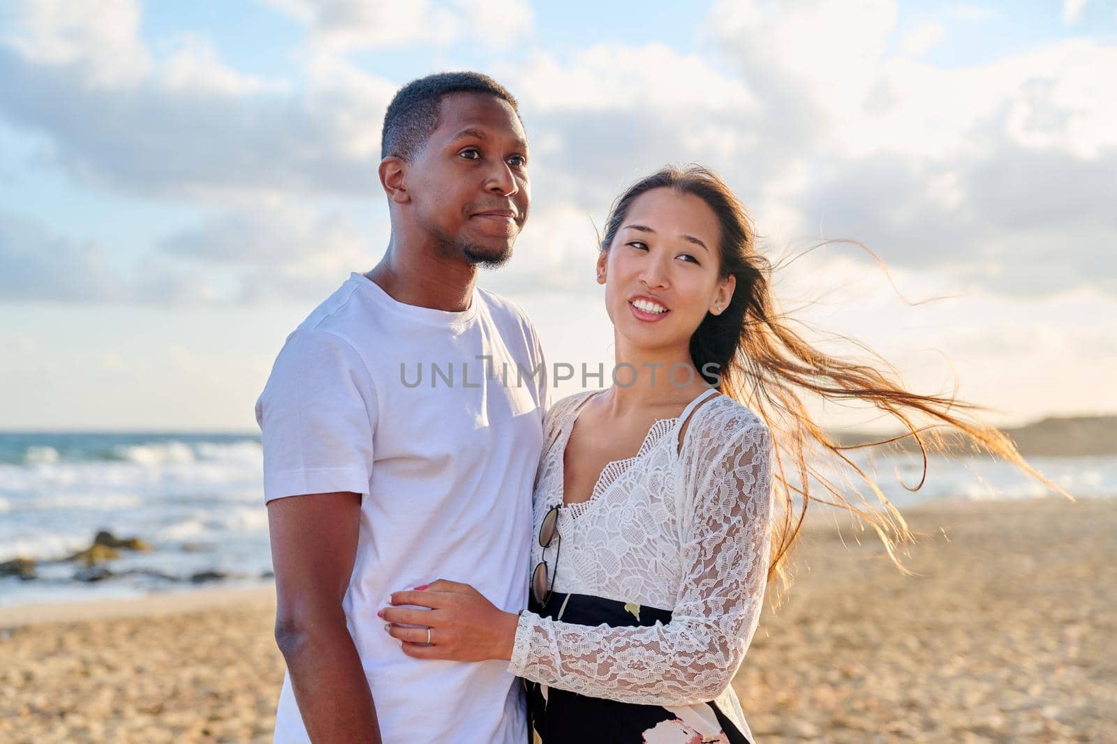 Loving romantic hugging young multiethnic couple on seashore. Happy african man and asian woman together. Love, relationship, dating, happiness, interracial family, tourism, travel, people concept
