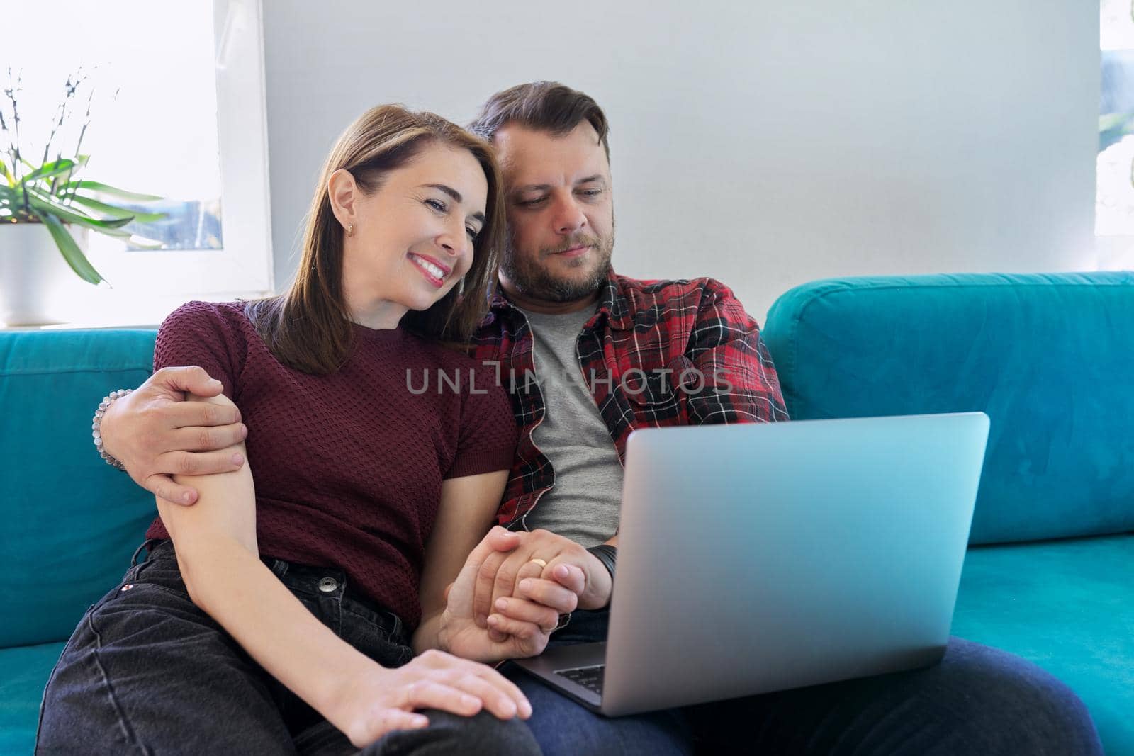 Happy middle aged couple sitting on couch with laptop by VH-studio