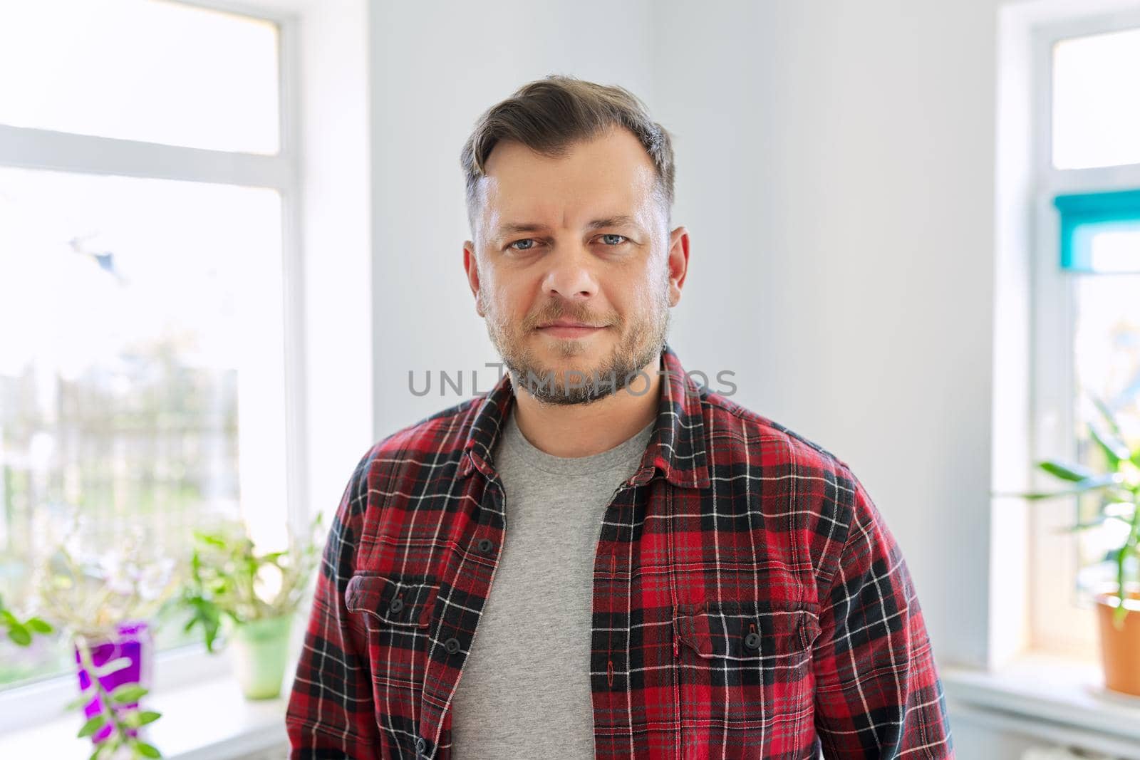 Portrait of 40 years old man, smiling male in plaid casual shirt looking at camera, home living room interior background