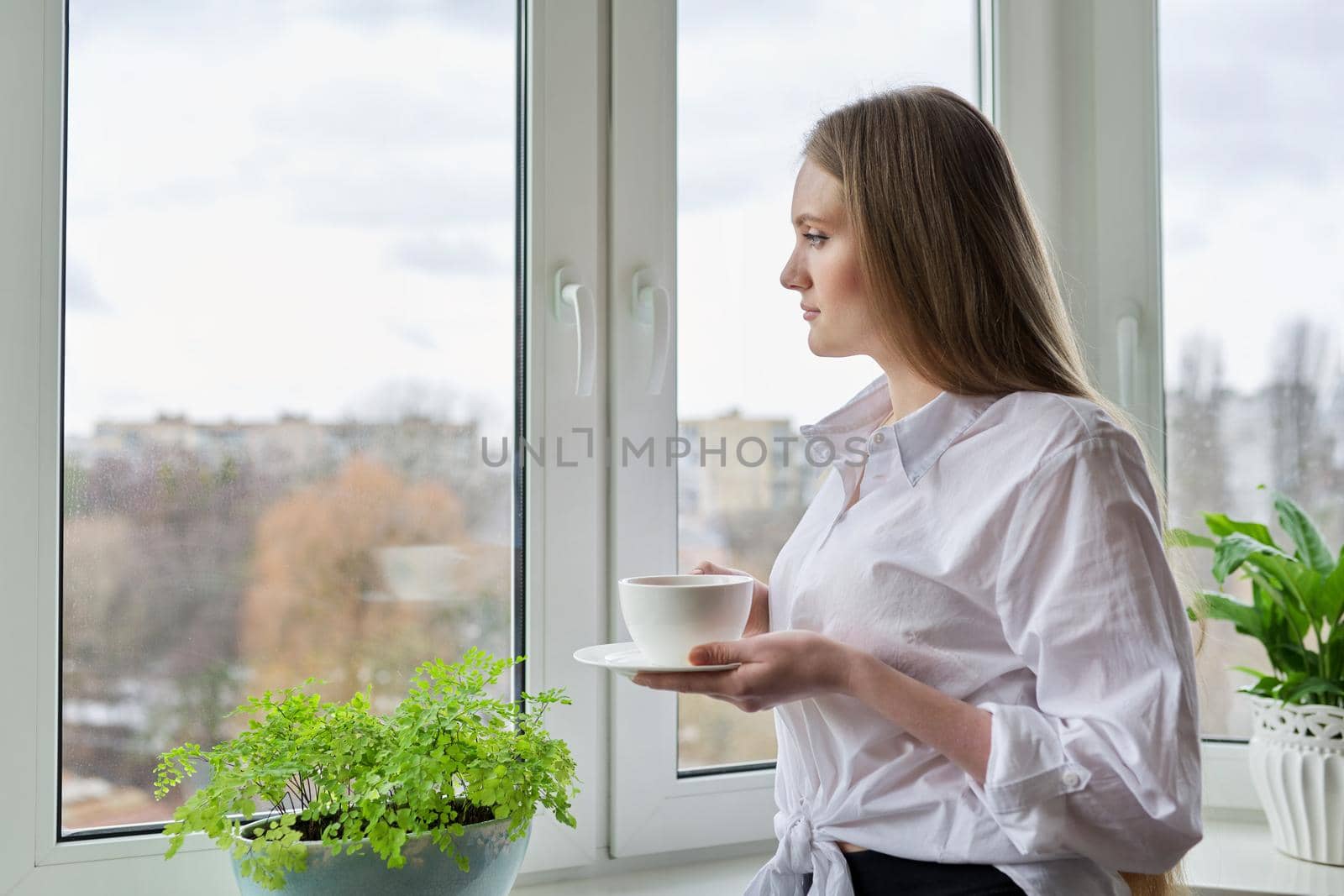 Portrait of young woman with cup of coffee near winter autumn window by VH-studio