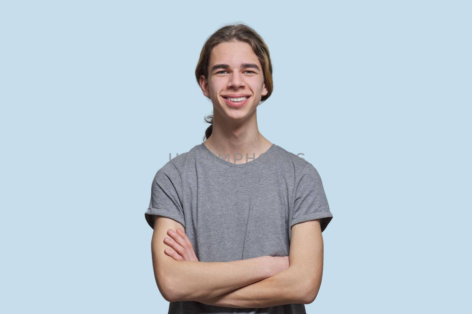 Portrait of happy smiling guy 15, 16 years old teenager with crossed arms, handsome trendy male looking at the camera on light studio background