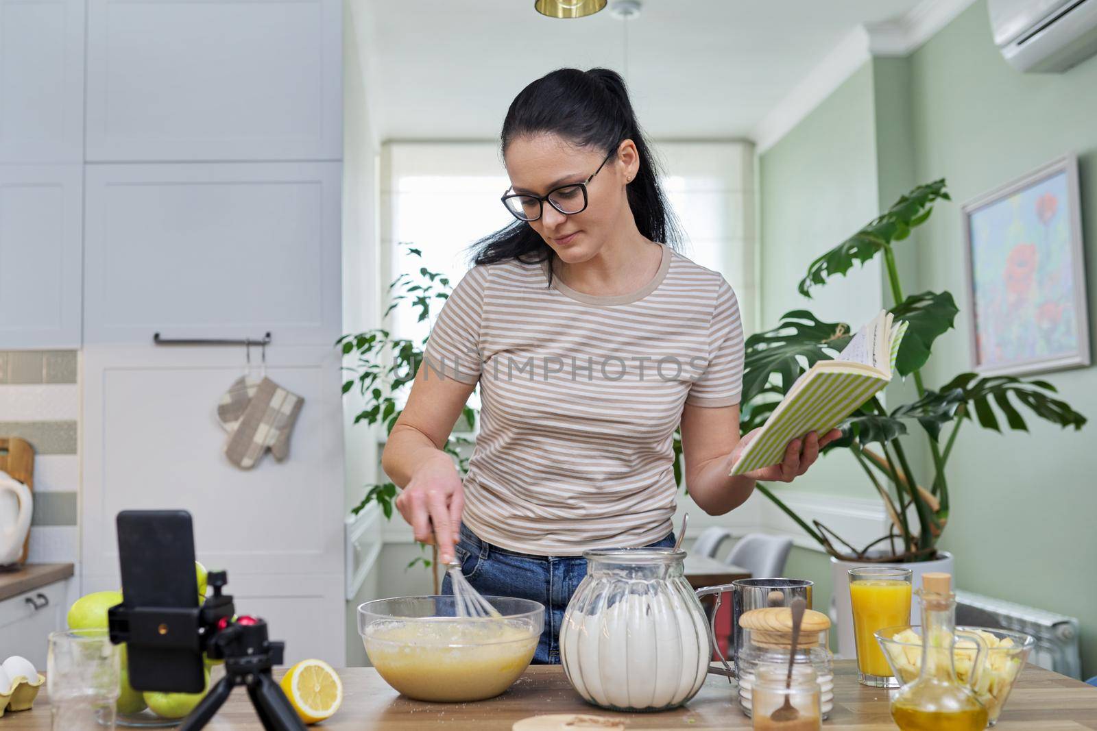 Woman preparing apple pie at home in kitchen, talking online using video call by VH-studio