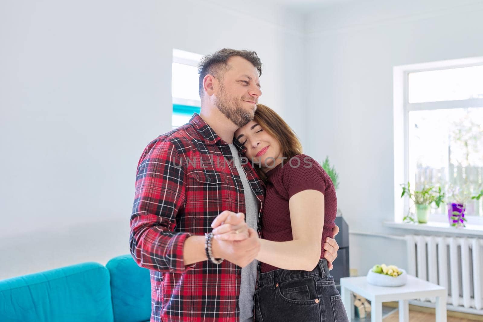 Happy romantic middle aged couple in love dancing, husband and wife dancing at home in living room, in home casual clothes. Relationships, lifestyle, communication, home life, middle-aged people