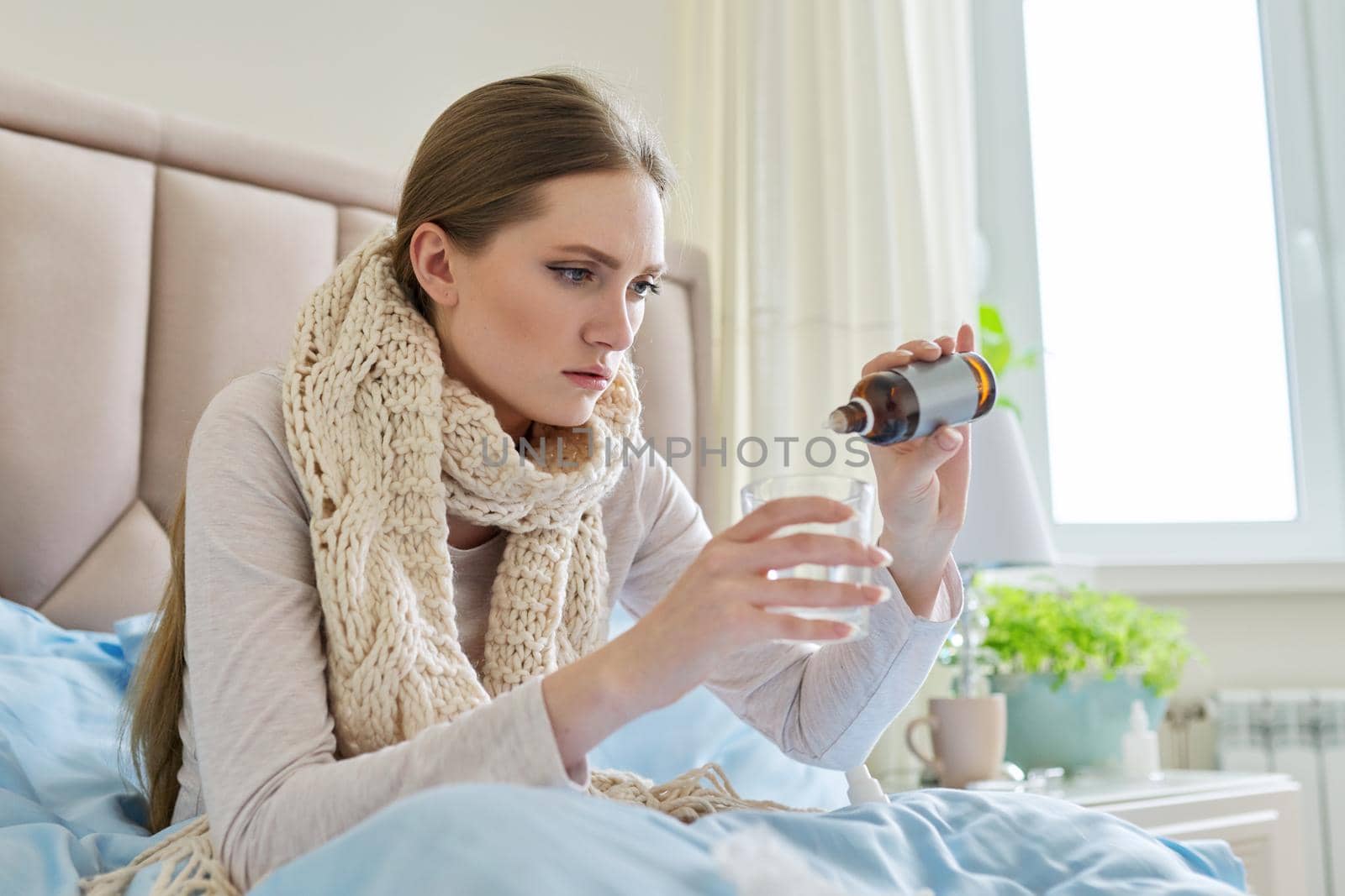 Sick woman at home in bed adding drops of medicine to a glass of water. Medicine, pharmacology, flu season, seasonal diseases, people concept