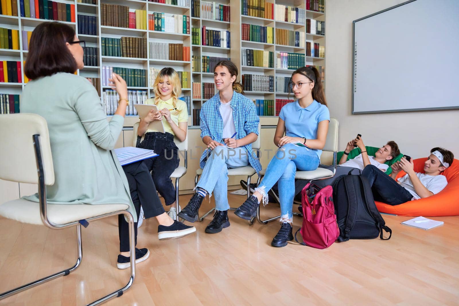 Female mentor teacher working with male teenage high school students in the library. Education, knowledge, adolescence, consultation, support, school, college concept