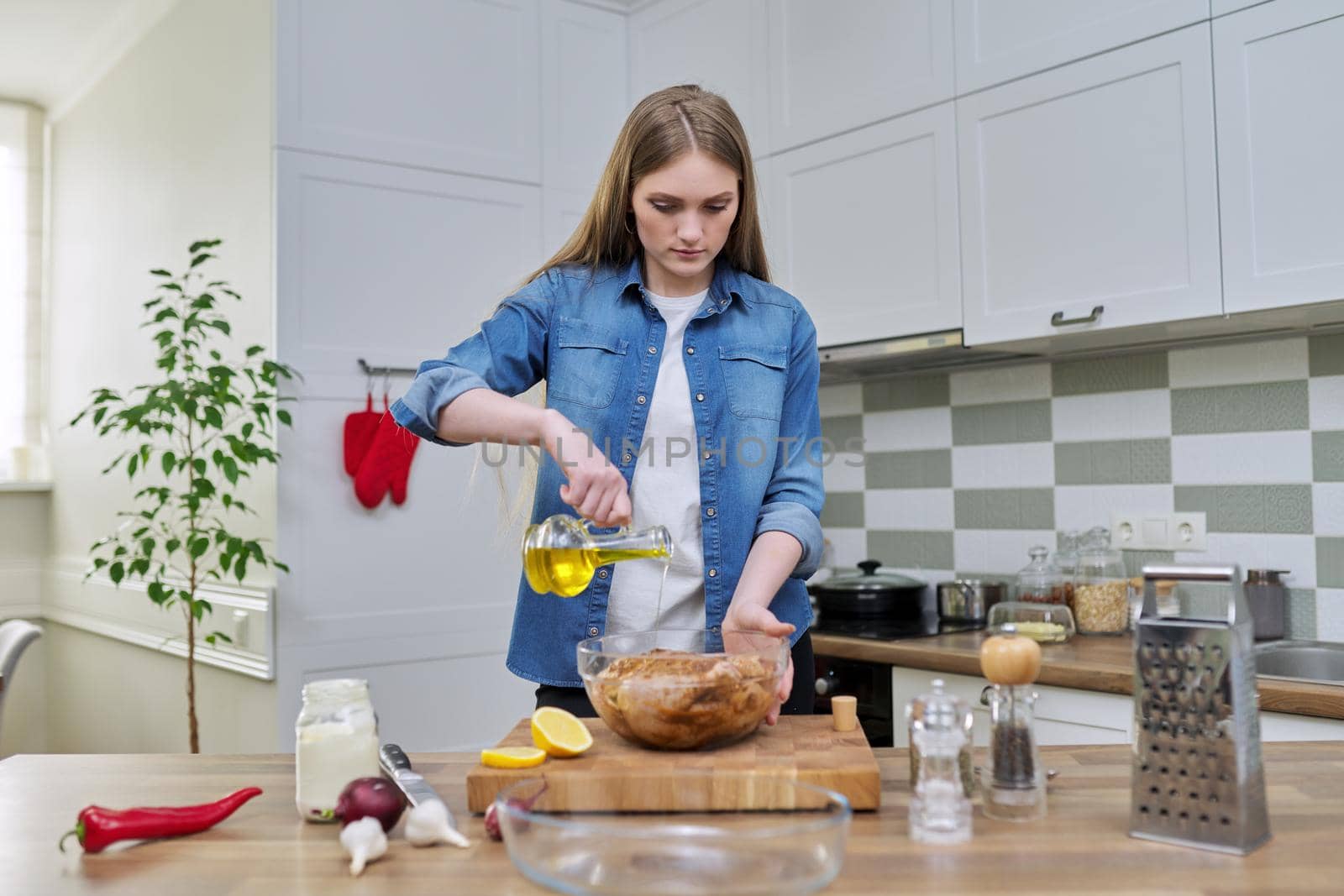 Young woman cooking chicken for the holiday, marinating with spices with black pepper, salt, olive oil and lemon, at home in the kitchen. Culinary blog, recipe, hobby and leisure.