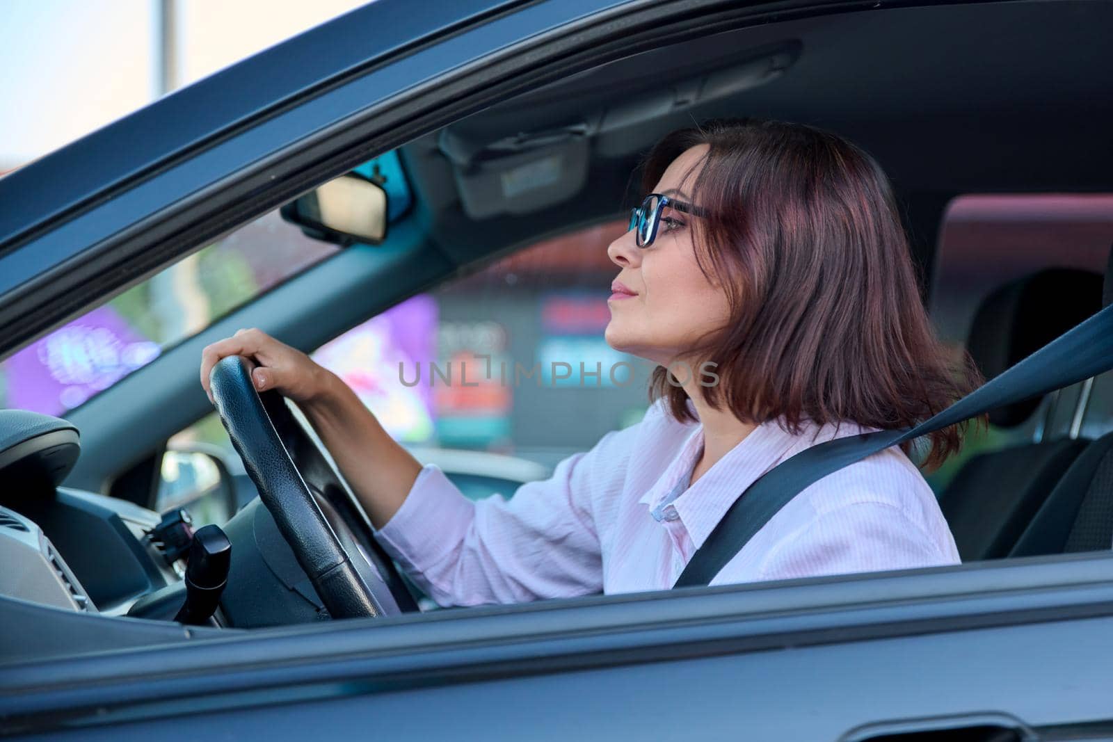 Middle-aged woman driver driving a car. Beautiful adult female with glasses, lifestyle, people, transport concept