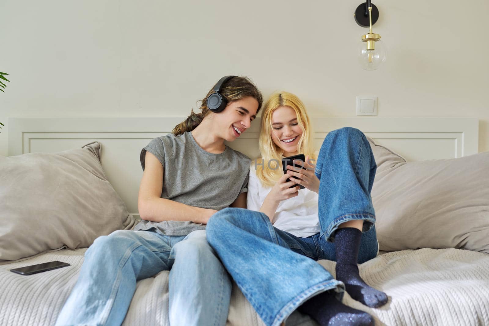 Happy laughing hipster teenagers male and female having fun using smartphone together. Couple using video call, watch funny photos videos. Lifestyle, technology, friendship, communication, adolescents