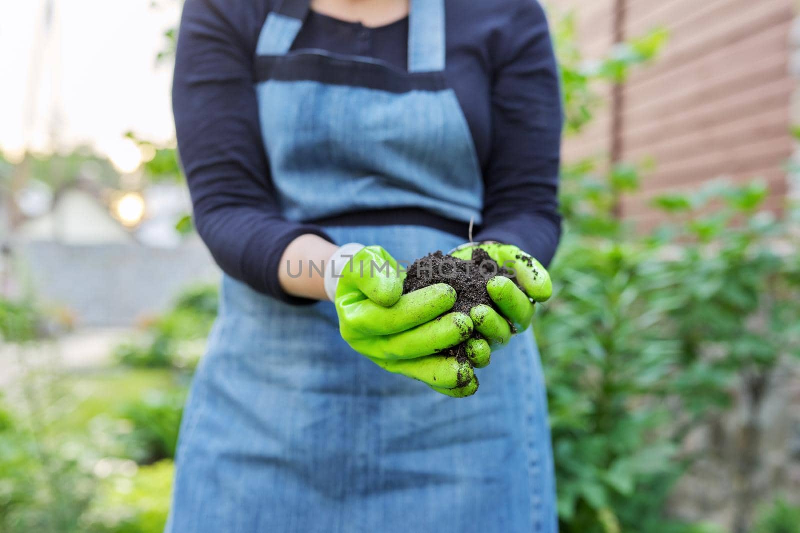 Close-up of woman's hand in gardening gloves with black fertile soil. Agriculture, horticulture, landscape, nature concept