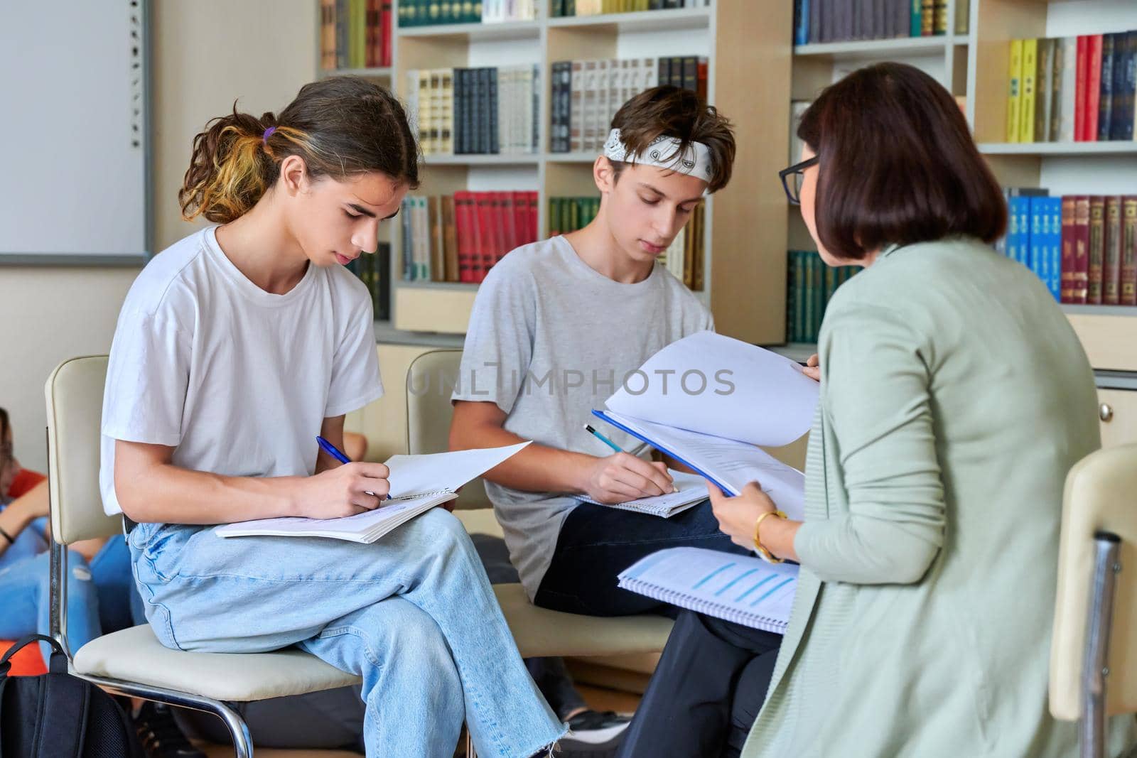 Female mentor teacher working with male teenage high school students in the library. Education, knowledge, adolescence, consultation, support, school, college concept