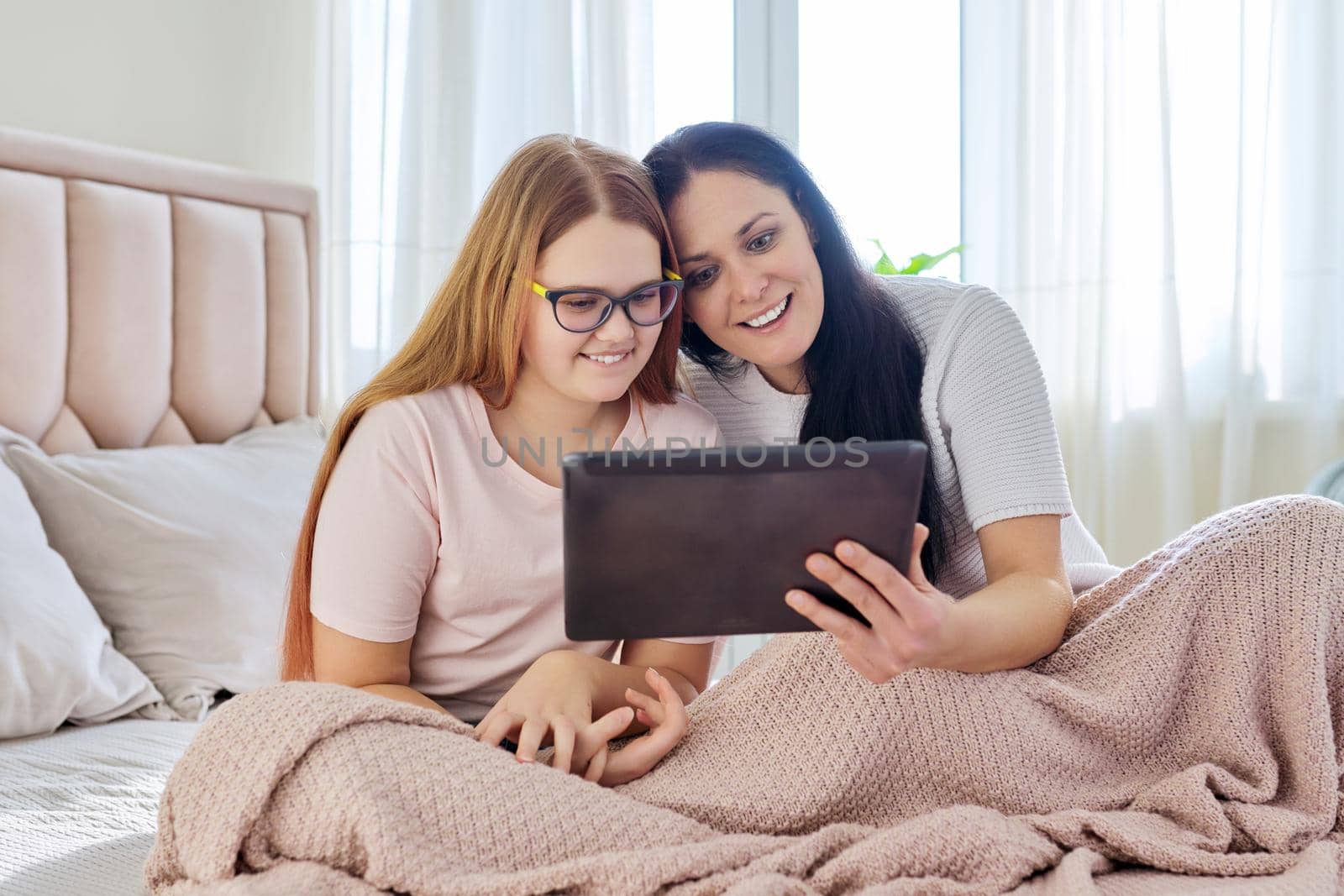 Communication relationship parent mom and child daughter teenager. Mother and daughter sitting together with digital tablet, looking at gadget screen, laughing, using video call, online meeting