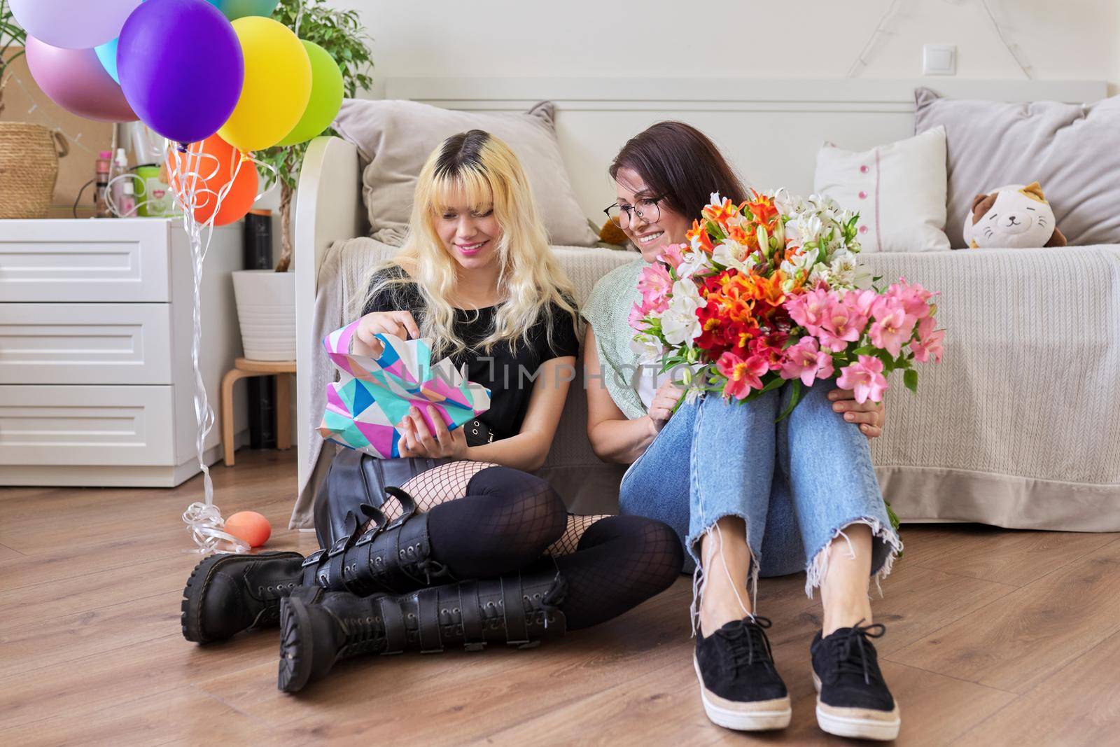 Mother and teen girl, happy birthday. Female mom congratulating daughter with bouquet of flowers and surprise gift box, room interior background. Holiday, celebration, parent teenager relationship