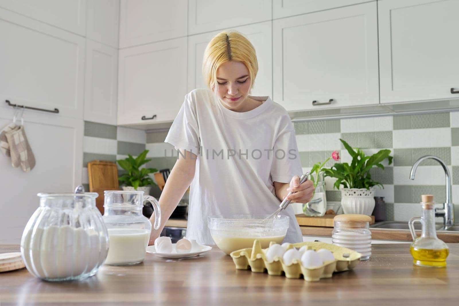 Female teenager preparing food at home, girl in the kitchen, ingredients for making pancakes eggs flour milk sugar on the table. Eating at home, healthy homemade food, teen hobbies