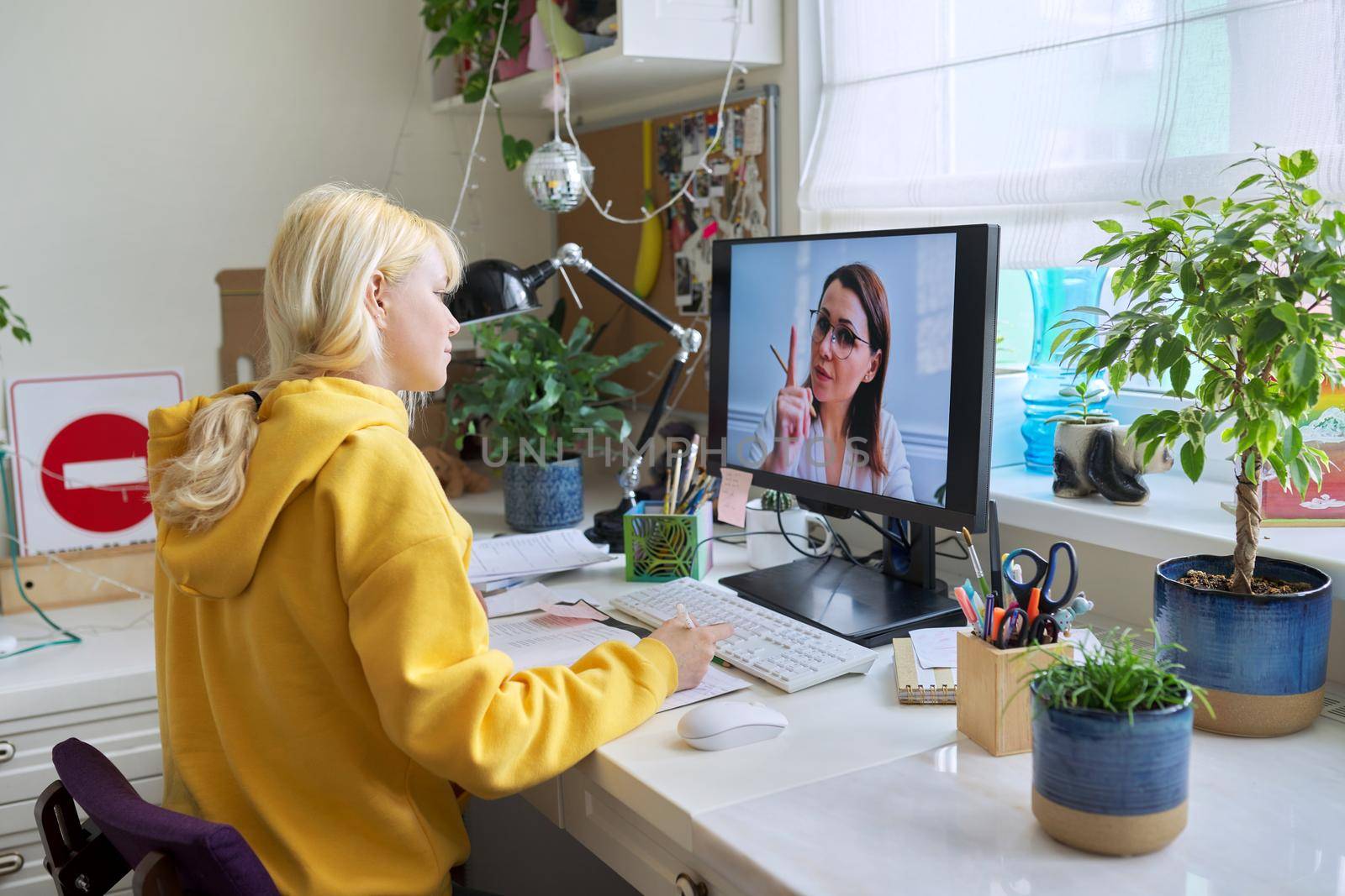 Teenager girl sitting at home studying online using home computer. Education and distance learning, video broadcast of lesson. Homeschooling, elearning, modern technologies in education