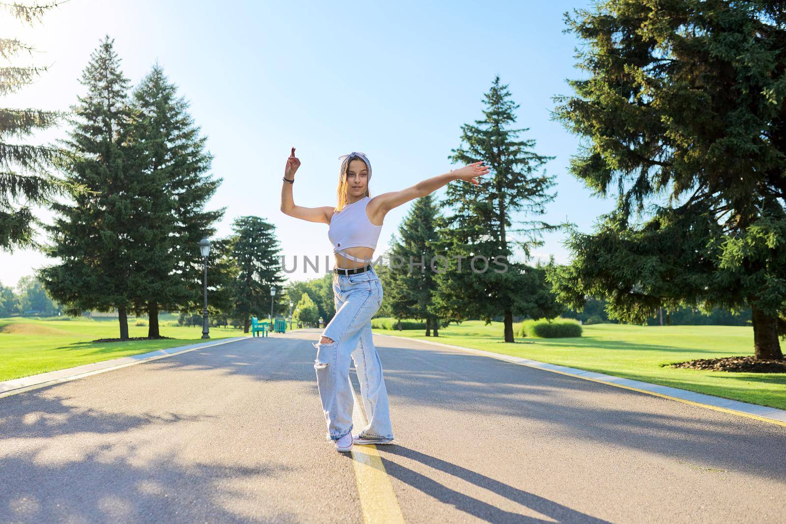 Dancing young female teenager on road in park on sunny summer day. Hipster teen girl in jeans dancing sports street dance. Youth, teens, summer, fashion, street style, lifestyle concept