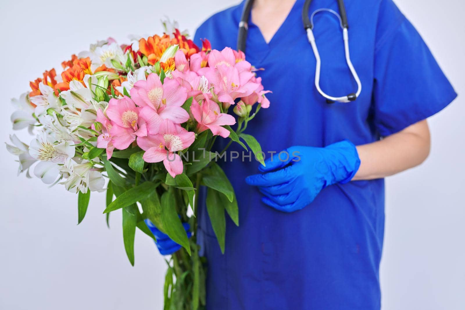 Health day, close-up bouquet of flowers in the hands of doctor nurse. Female medic in blue medical uniform, protective gloves with stethoscope on light background