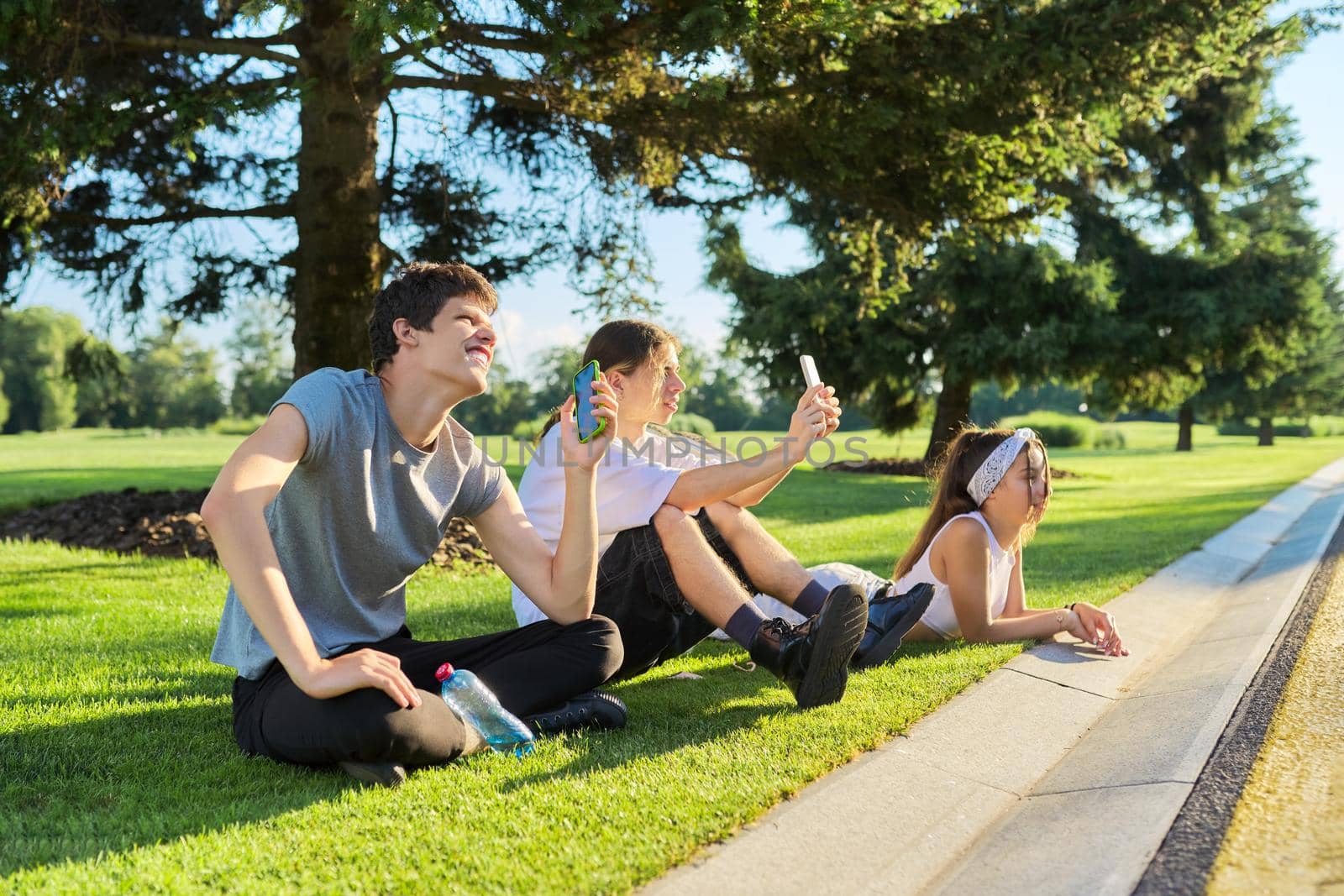 Hipster teenagers having fun in park, sitting on green grass on lawn, recording videos on smartphone by VH-studio