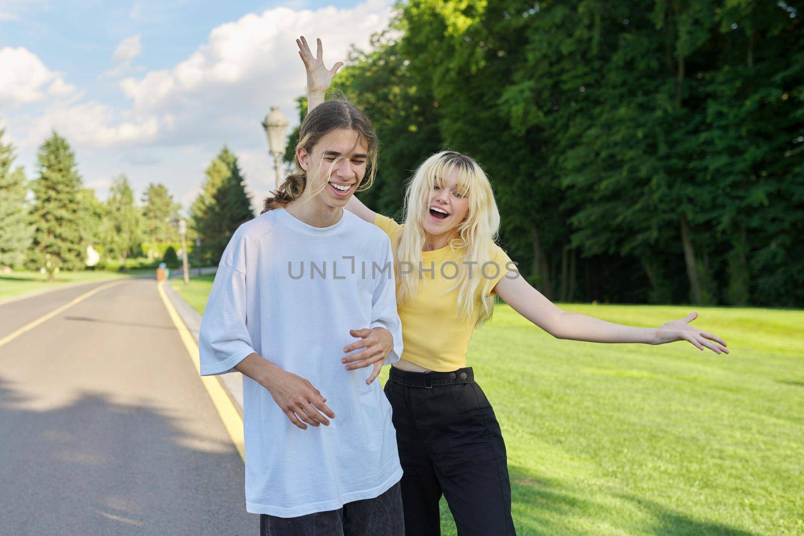 Happy teenagers filming video on smartphone. Laughing dancing singing couple of teenagers looking at smartphone screen and recording videos for social media, young bloggers vloggers