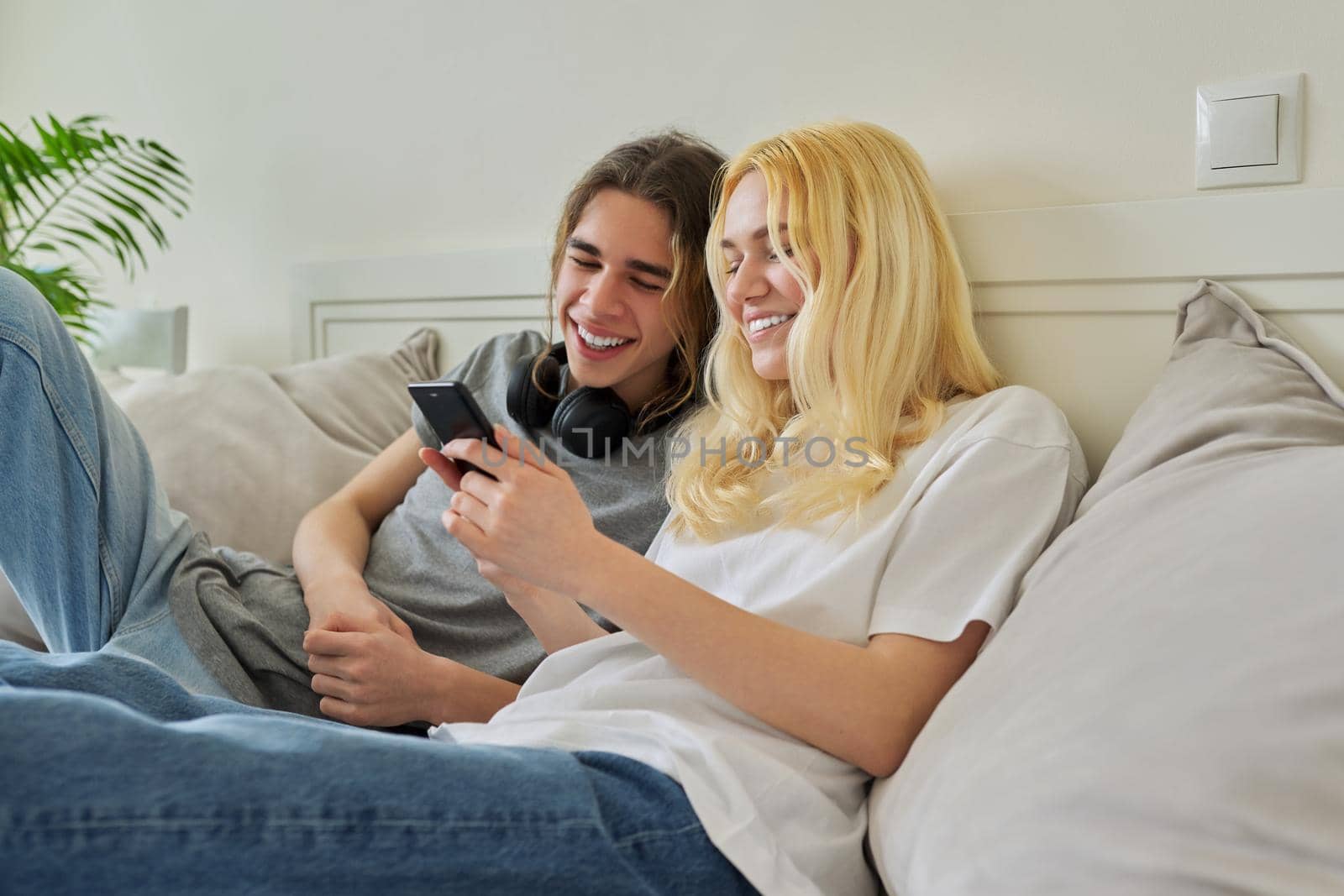 Happy laughing hipster teenagers male and female having fun using smartphone together. Couple using video call, watch funny photos videos. Lifestyle, technology, friendship, communication, adolescents