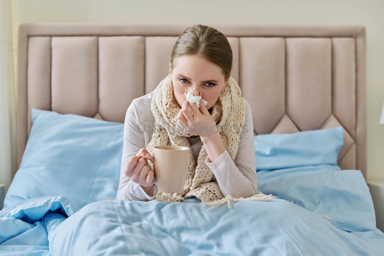 Sick young woman in bed with handkerchief and cup by VH-studio