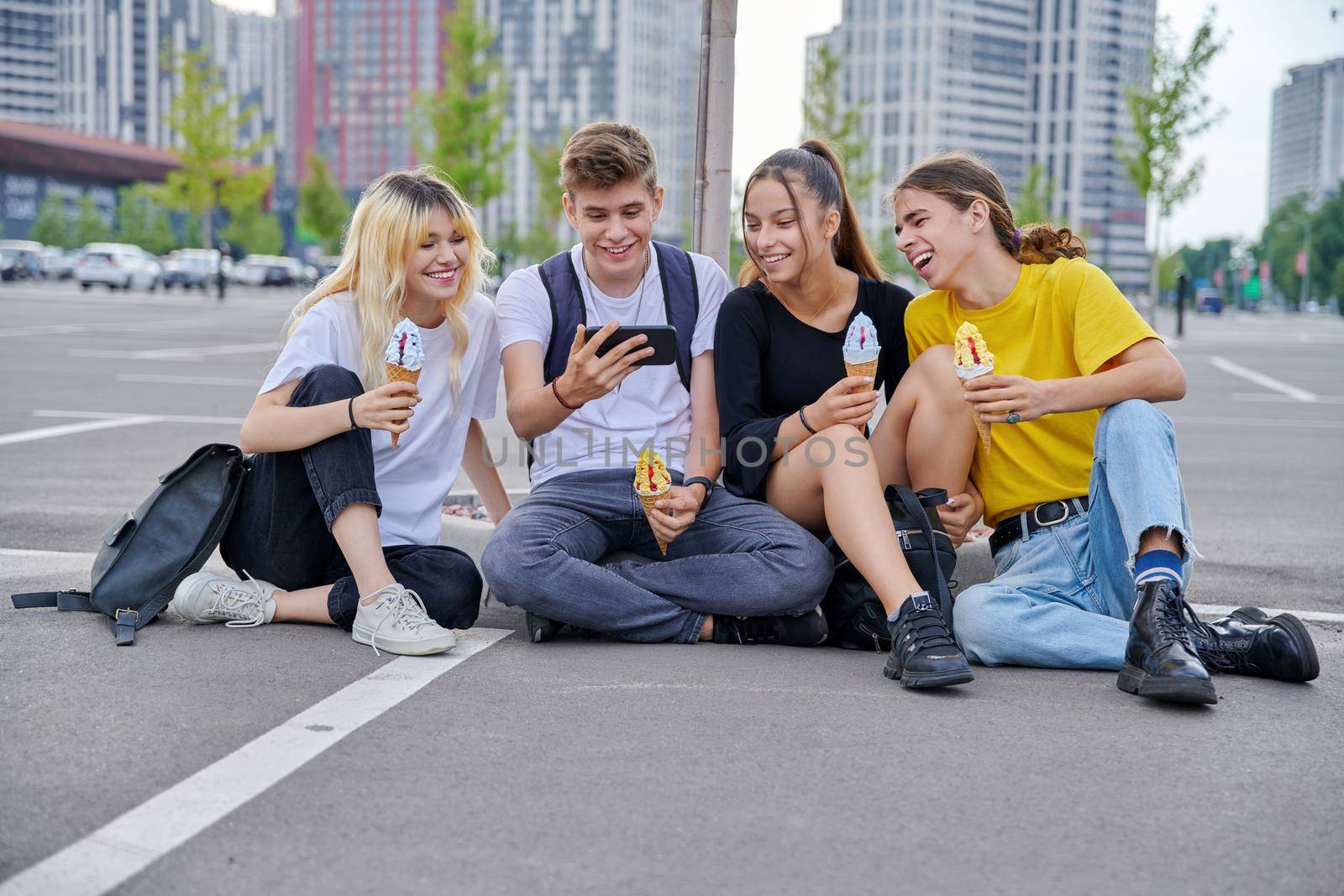 Group of teenagers with ice cream looking together at smartphone screen, urban style, modern city background. Trending youth, friendship, lifestyle, fun, adolescence concept