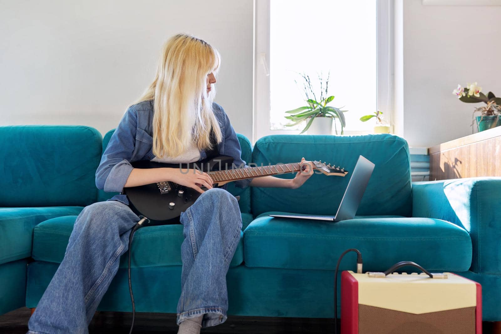 Hipster teenager girl playing electric guitar looking at laptop. Online learning music, songs, self-education, teen blogger musician recording video blog vlog, teaching, taking musical online courses