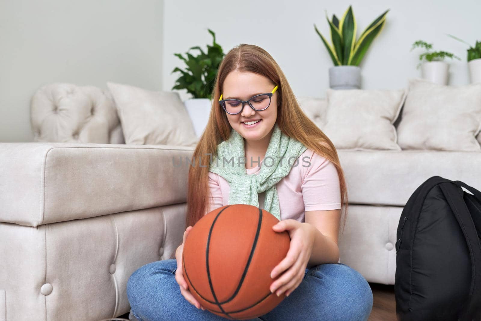 Happy smiling teenage girl with basketball ball in hands sitting on floor at home. Active healthy sports lifestyle for adolescents and teenagers