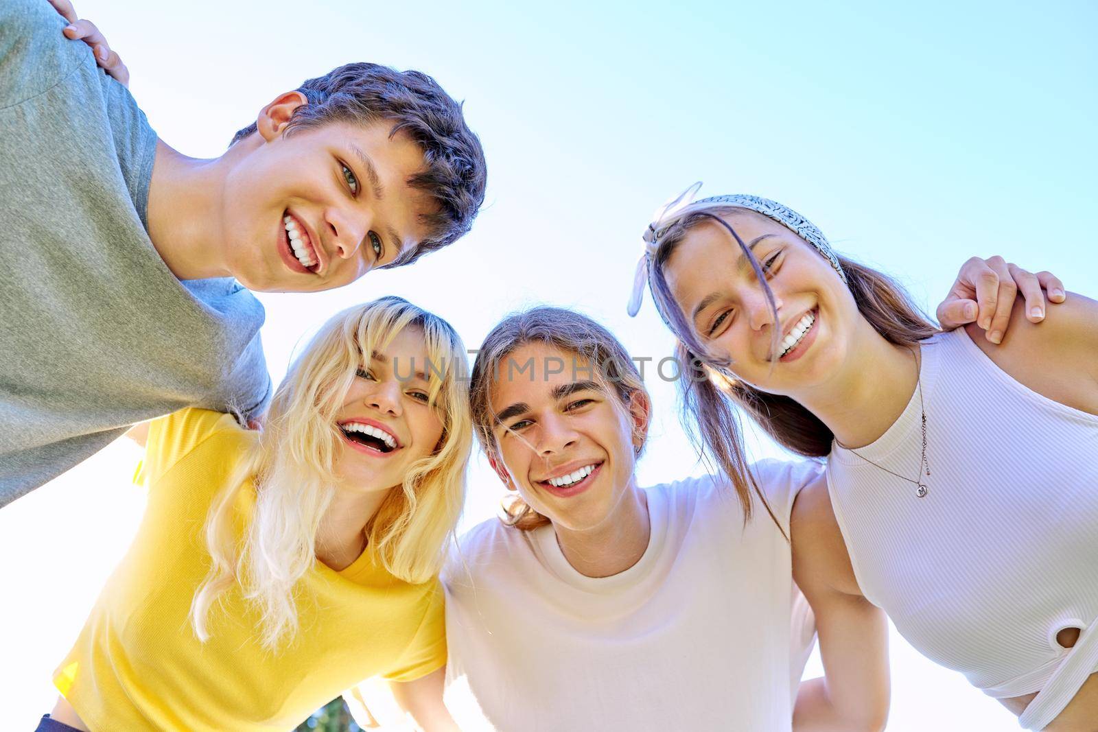 Close-up of happy smiling teenage faces. Hugging teenagers looking at the camera, sky background. by VH-studio