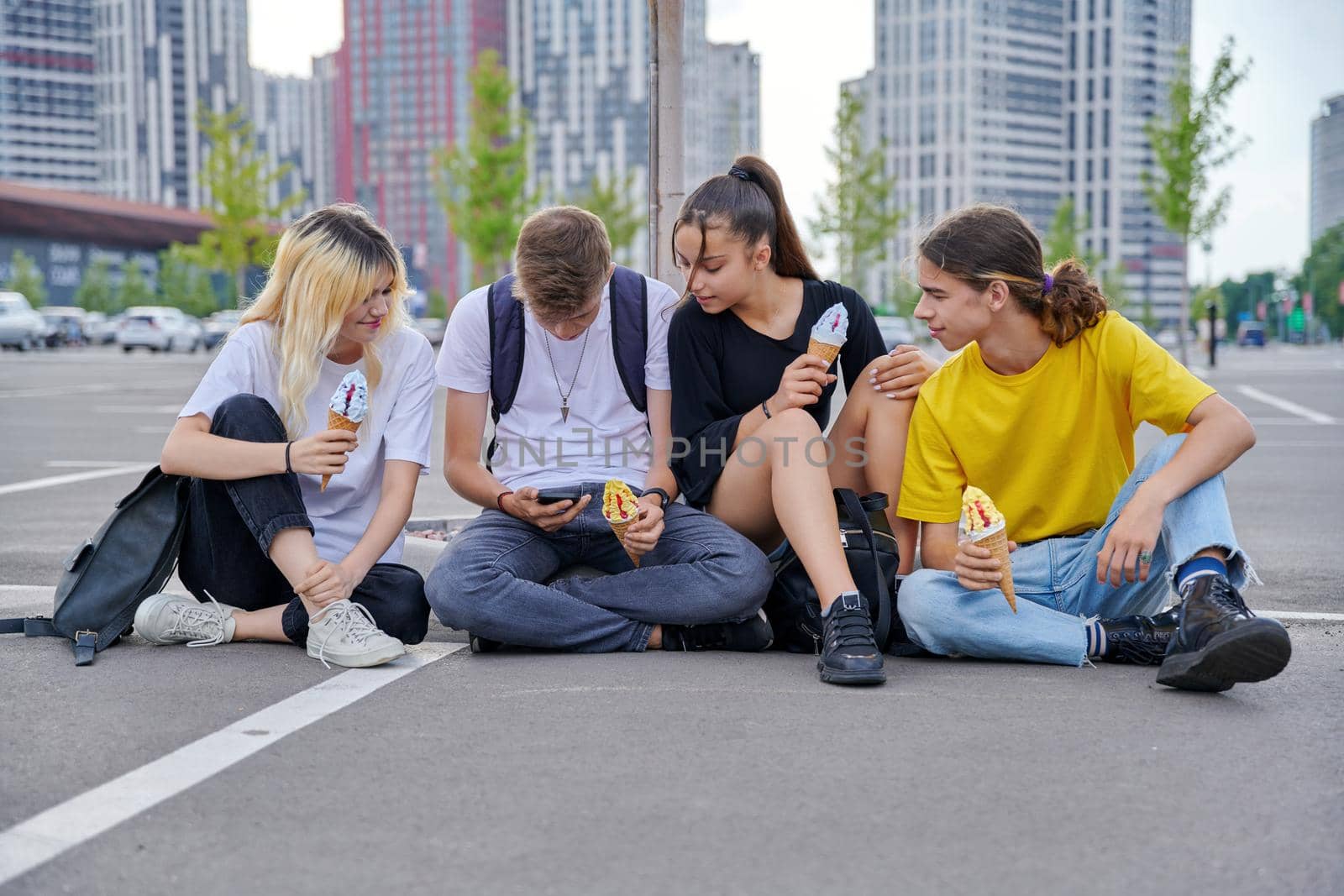 Group of teenagers with ice cream looking together at smartphone, urban style by VH-studio