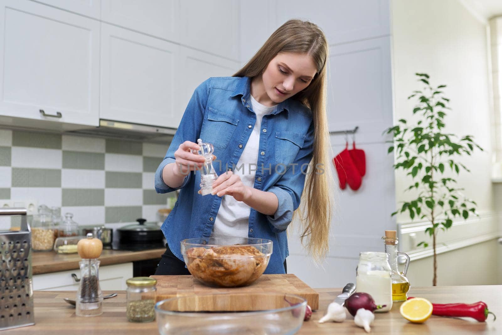 Young woman cooking chicken for holiday, marinating with spices with black pepper salt, at home in kitchen. Culinary blog, recipe, hobby and leisure.