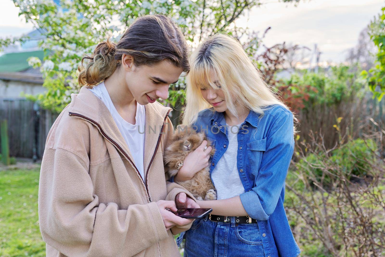 Teenagers with decorative rabbit in hands talking and looking at smartphone by VH-studio