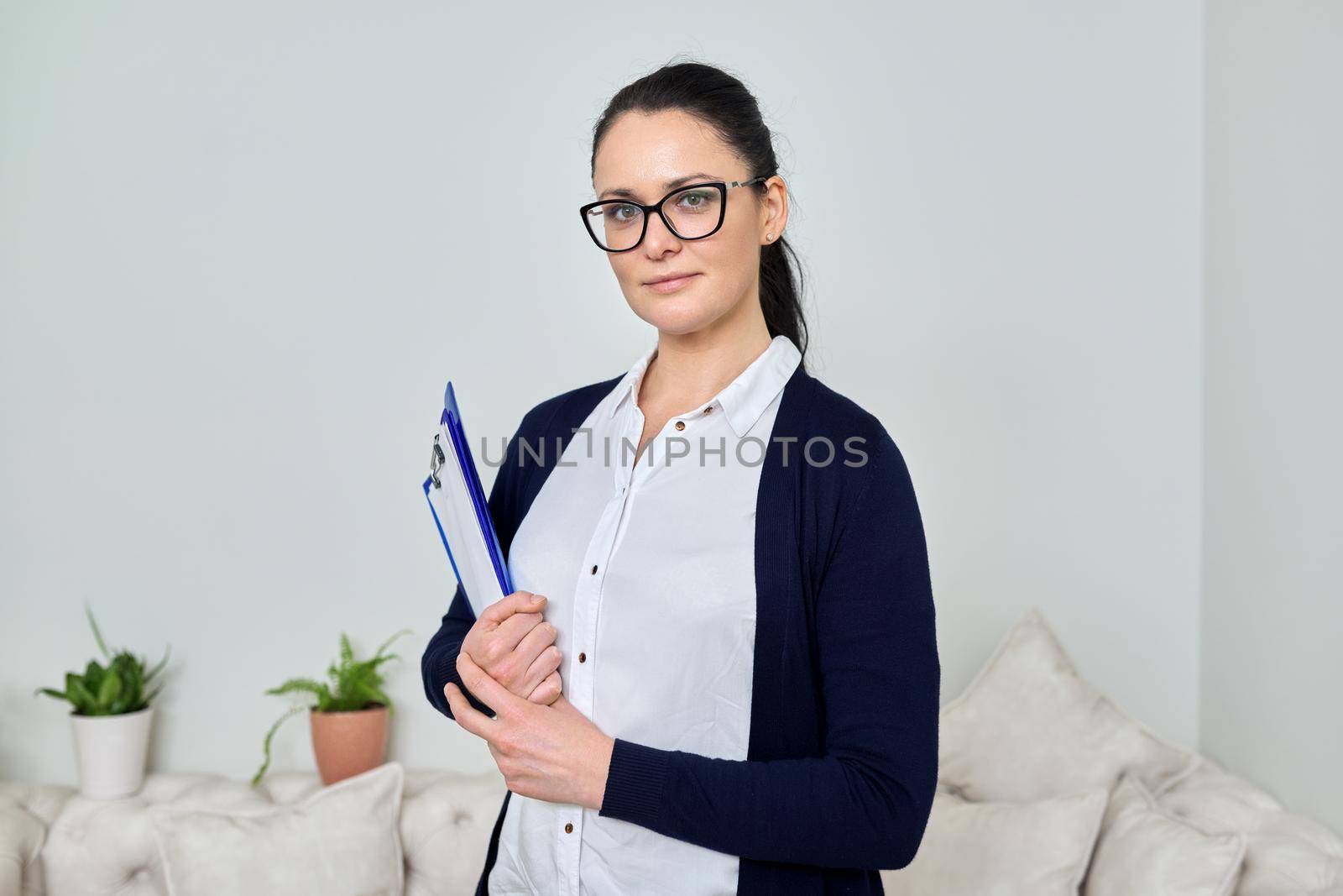 Portrait of smiling successful business woman 40 years old wearing glasses with papers in her hands looking at camera