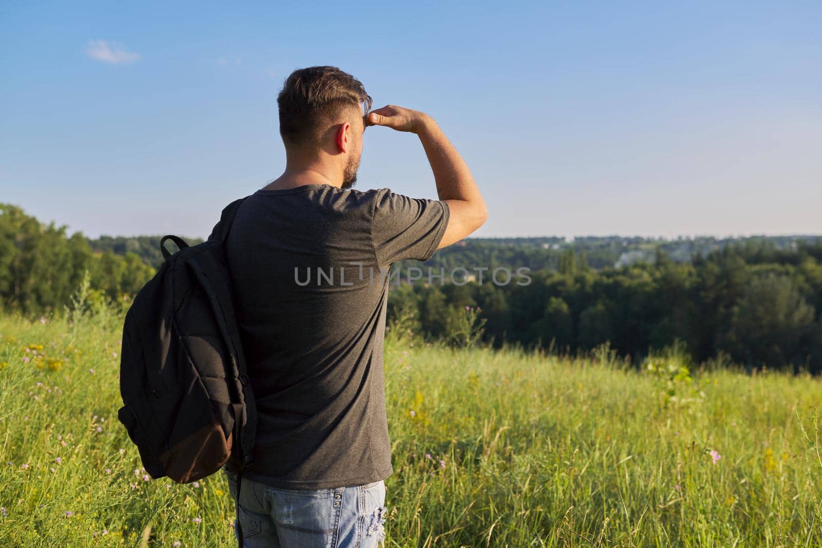 Back view of middle-aged man with backpack looking in distance at natural hills, meadows, sky. Hike, travel, summer, active lifestyle, people 40s age concept