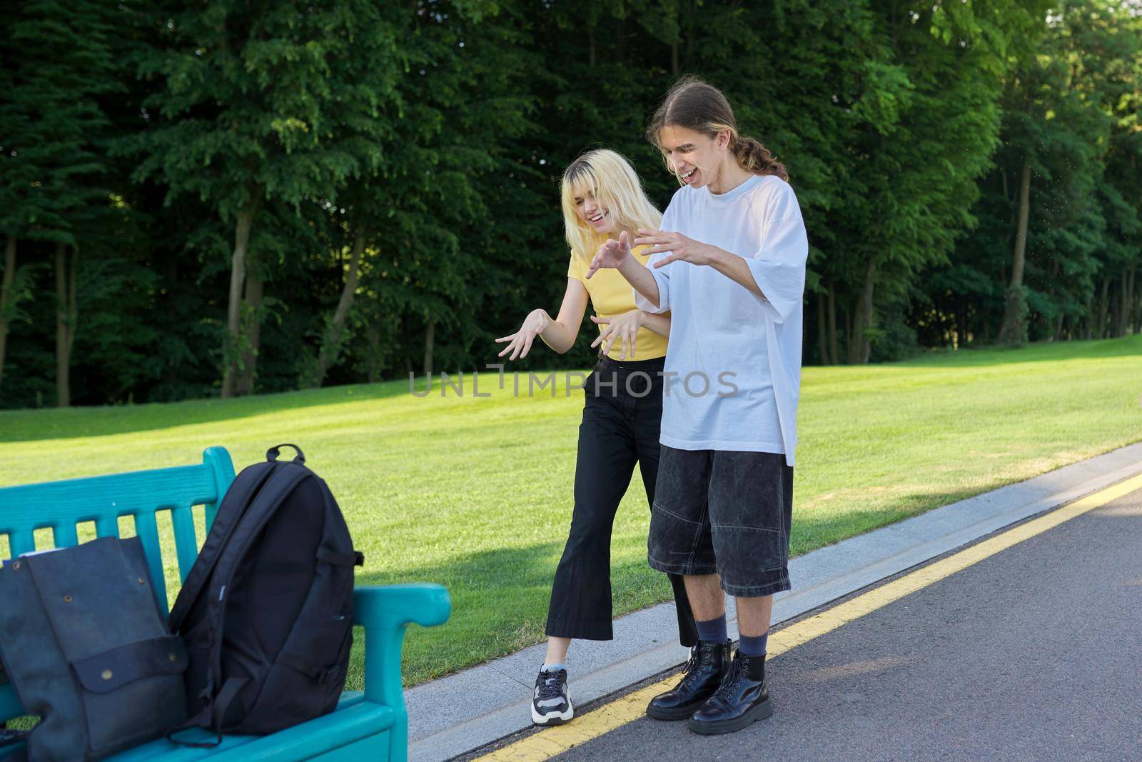 Happy teenagers filming video on smartphone. Laughing dancing singing couple of teenagers looking at smartphone screen and recording videos for social media, young bloggers vloggers