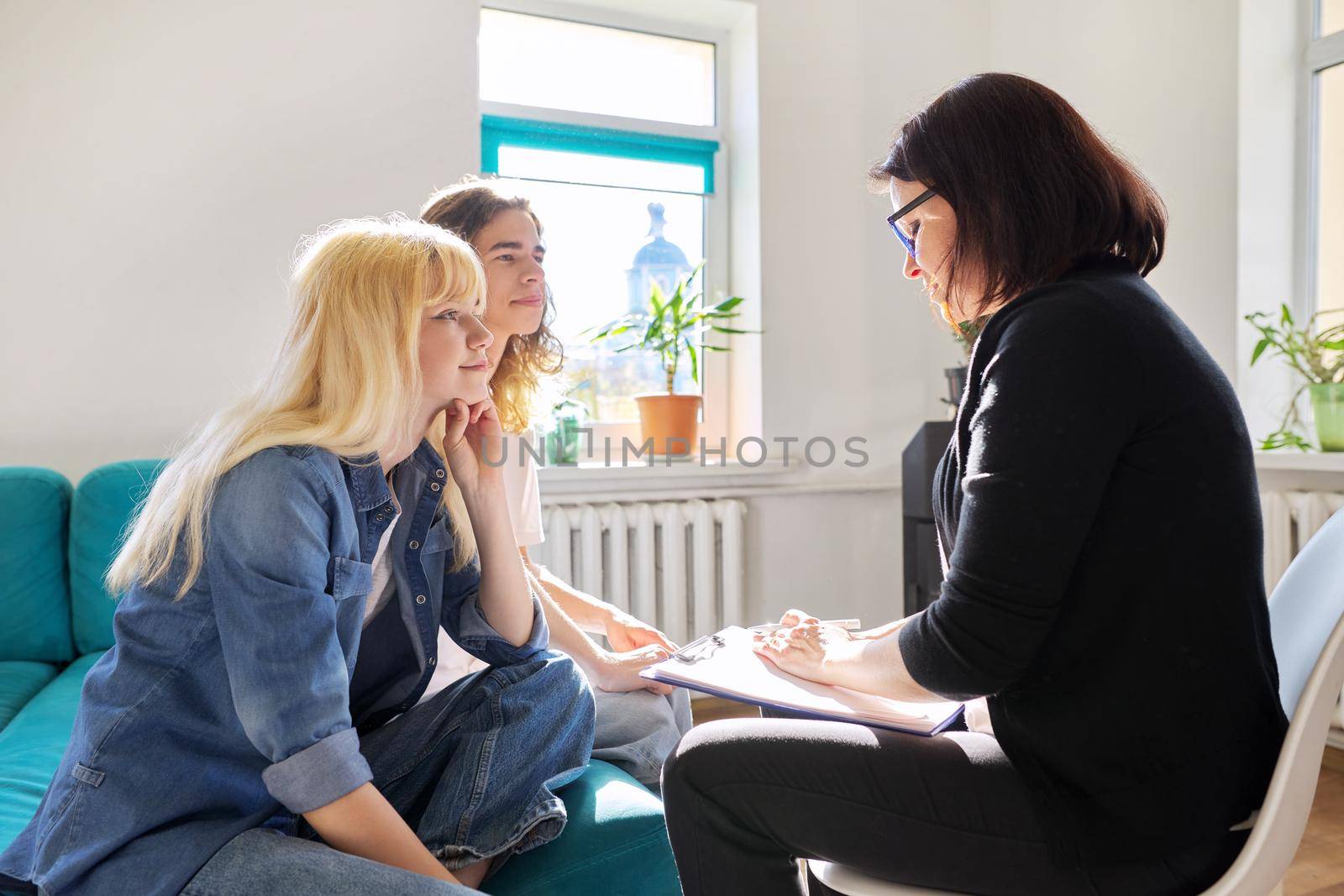 Teenagers guy and girl 16, 17 years old at meeting with teacher, school psychologist, counselor, sitting together talking, discussing. Professional help for adolescents, social issues, help in studies