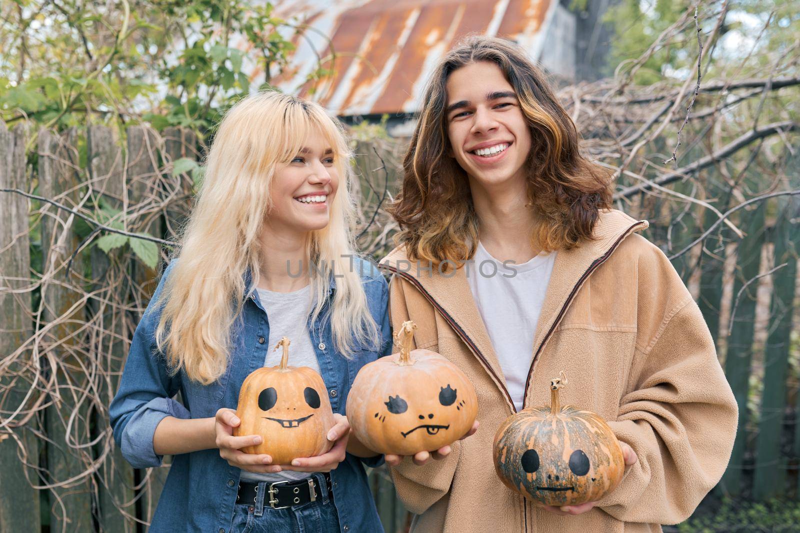 Couple of laughing teenagers with pumpkins having fun outdoors in the garden, halloween autumn holiday, youth concept