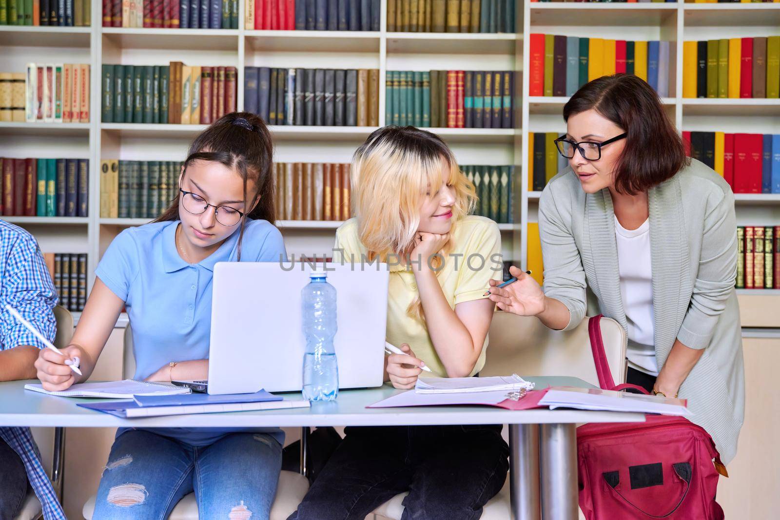 Girls teenage students studying in library with female teacher mentor. High school, education, adolescent, back to school, back to college concept