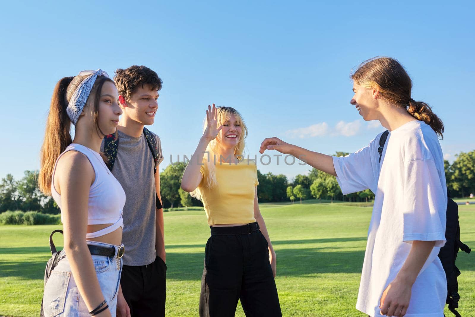 Meeting of teenage friends. Group of cheerful happy teenagers walking along road on sunny summer day. Adolescence, youth, friendship, young people concept