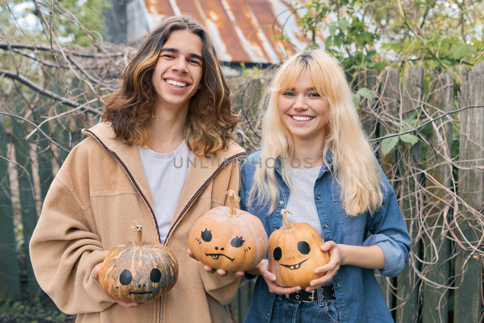 Couple of laughing teenagers with pumpkins having fun outdoors in the garden, halloween autumn holiday, youth concept