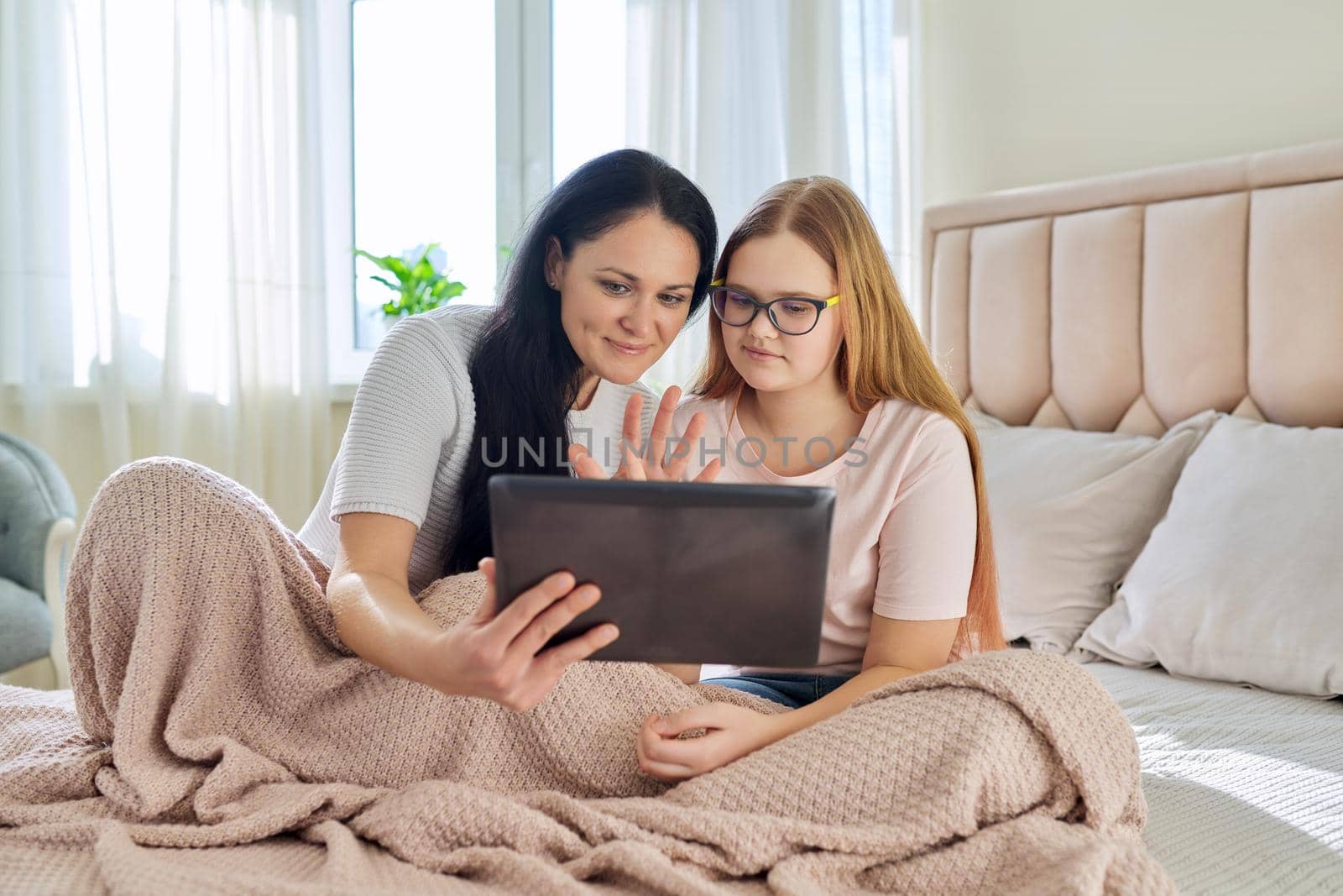 Communication relationship parent mom and child daughter teenager. Mother and daughter sitting together with digital tablet, looking at gadget screen, laughing, using video call, online meeting
