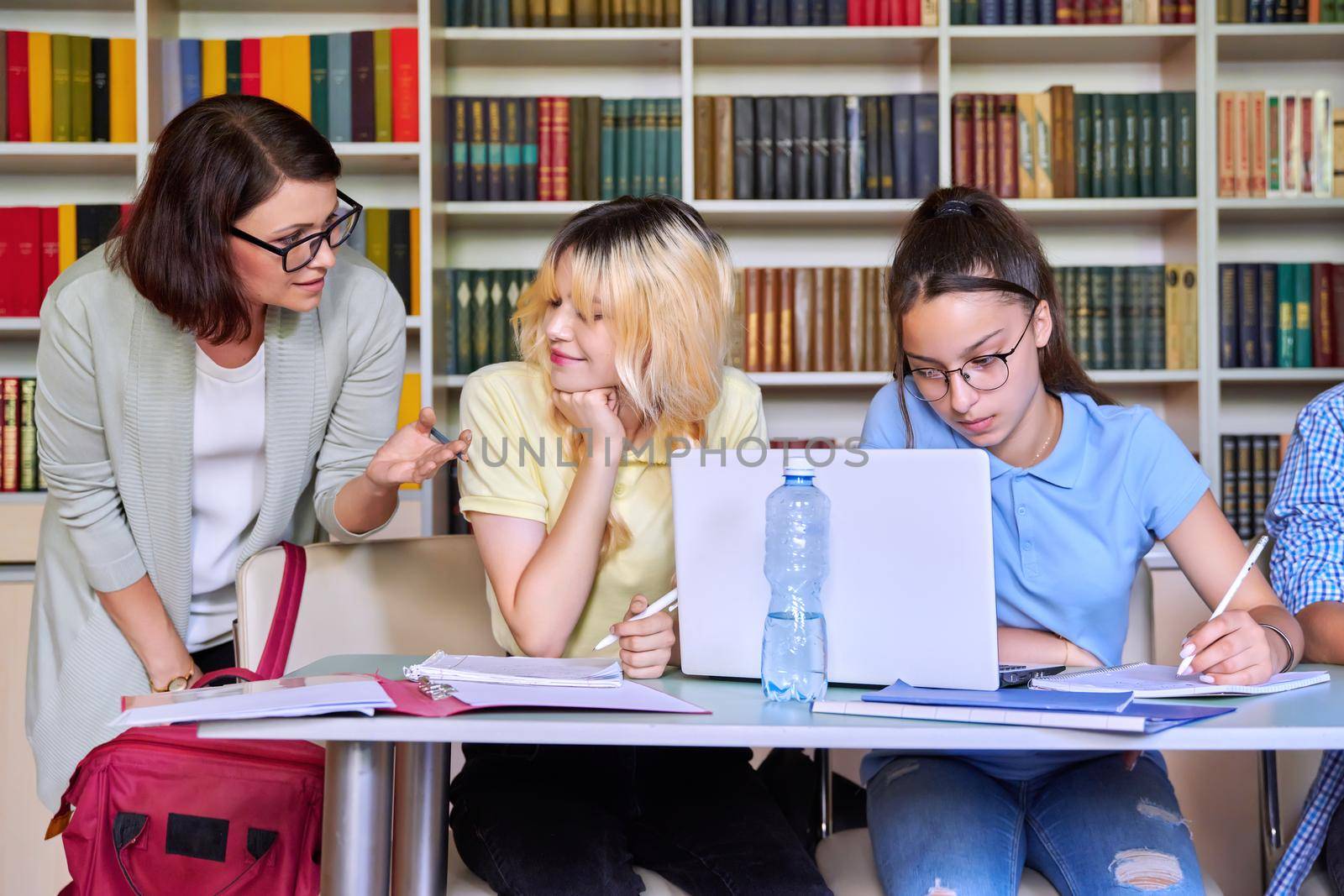 Girls teenage students studying in library with female teacher mentor. High school, education, adolescent, back to school, back to college concept
