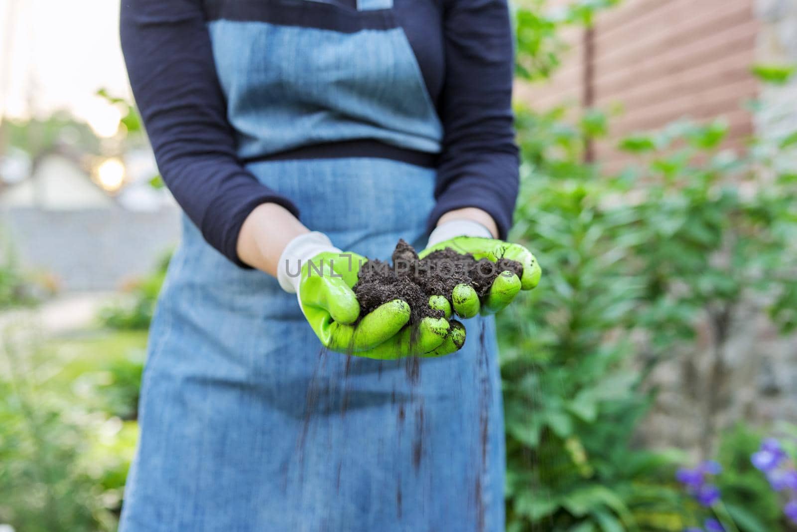 Close-up of woman's hand in gardening gloves with black fertile soil. Agriculture, horticulture, landscape, nature concept