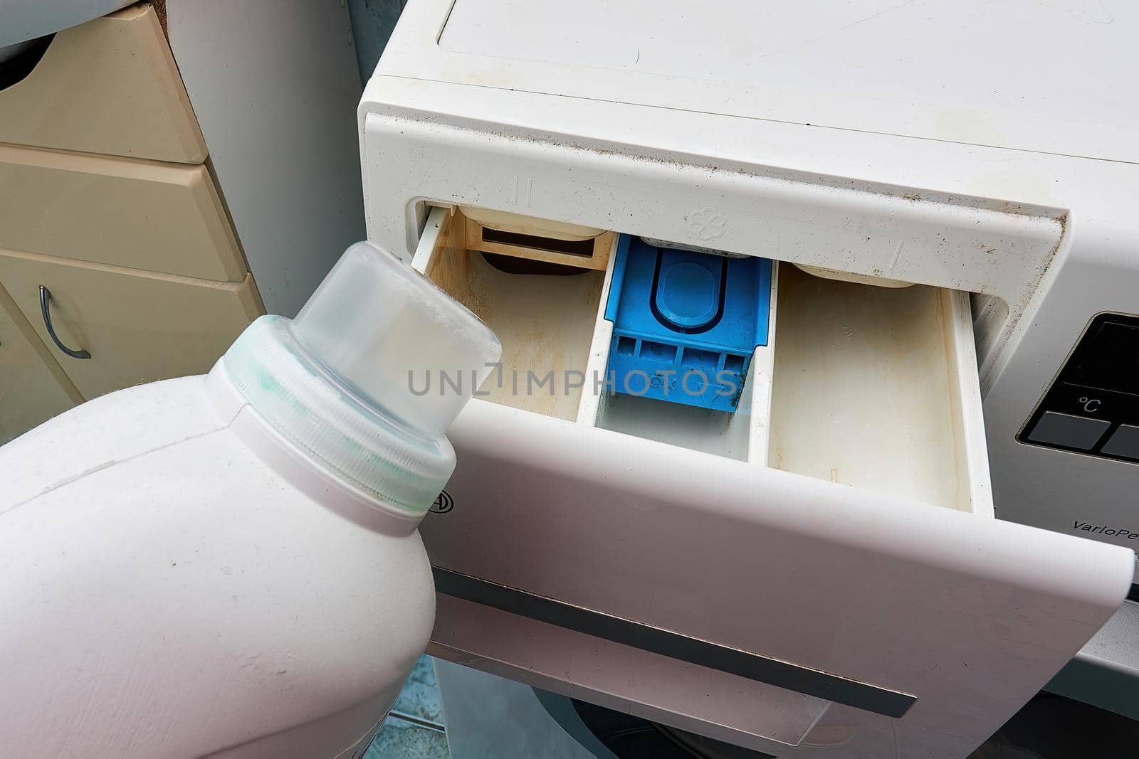 White plastic bottle with detergent against the background of the open compartment of the washing machine, close up.