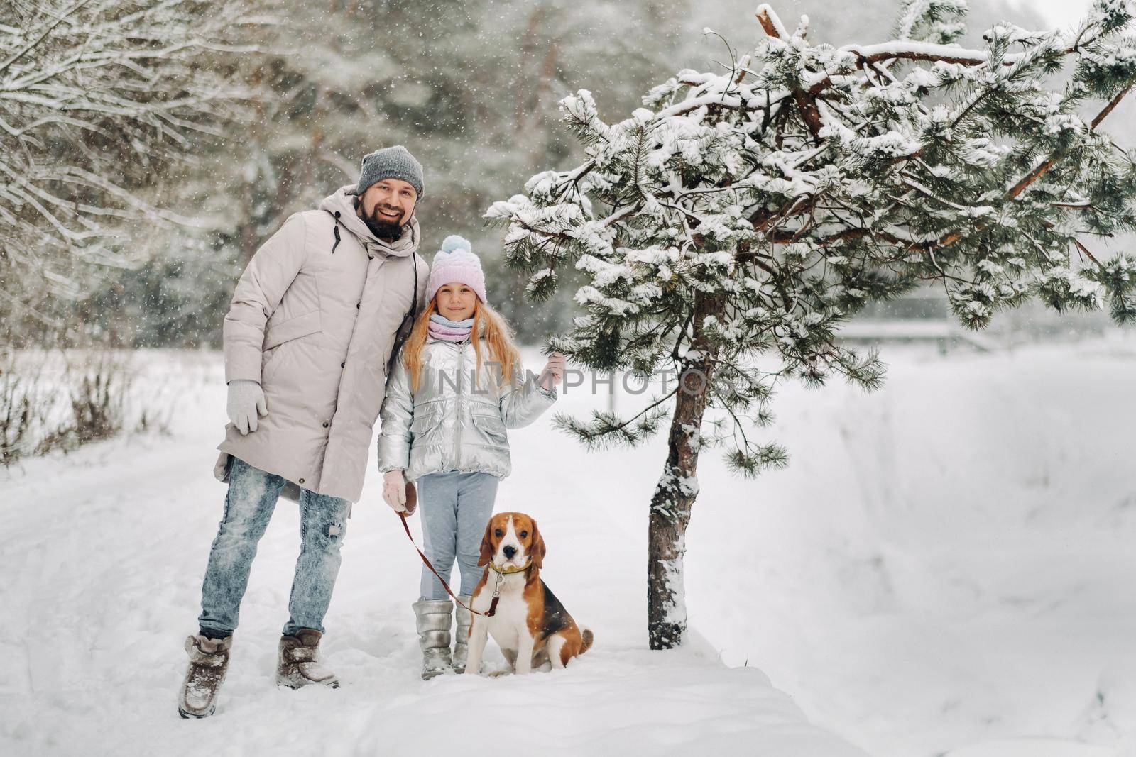 Family father and daughter on a walk with their dog in the winter forest.