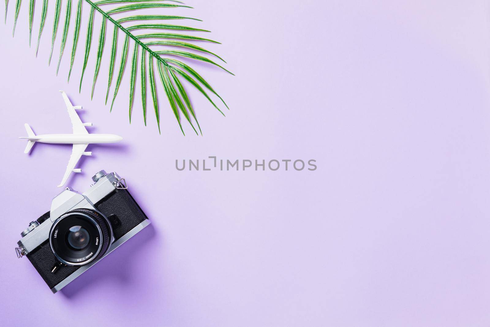 Top view flat lay mockup of retro camera films, airplane, leaves and traveler accessories isolated on a purple background with copy space, Business trip, and vacation summer travel concept