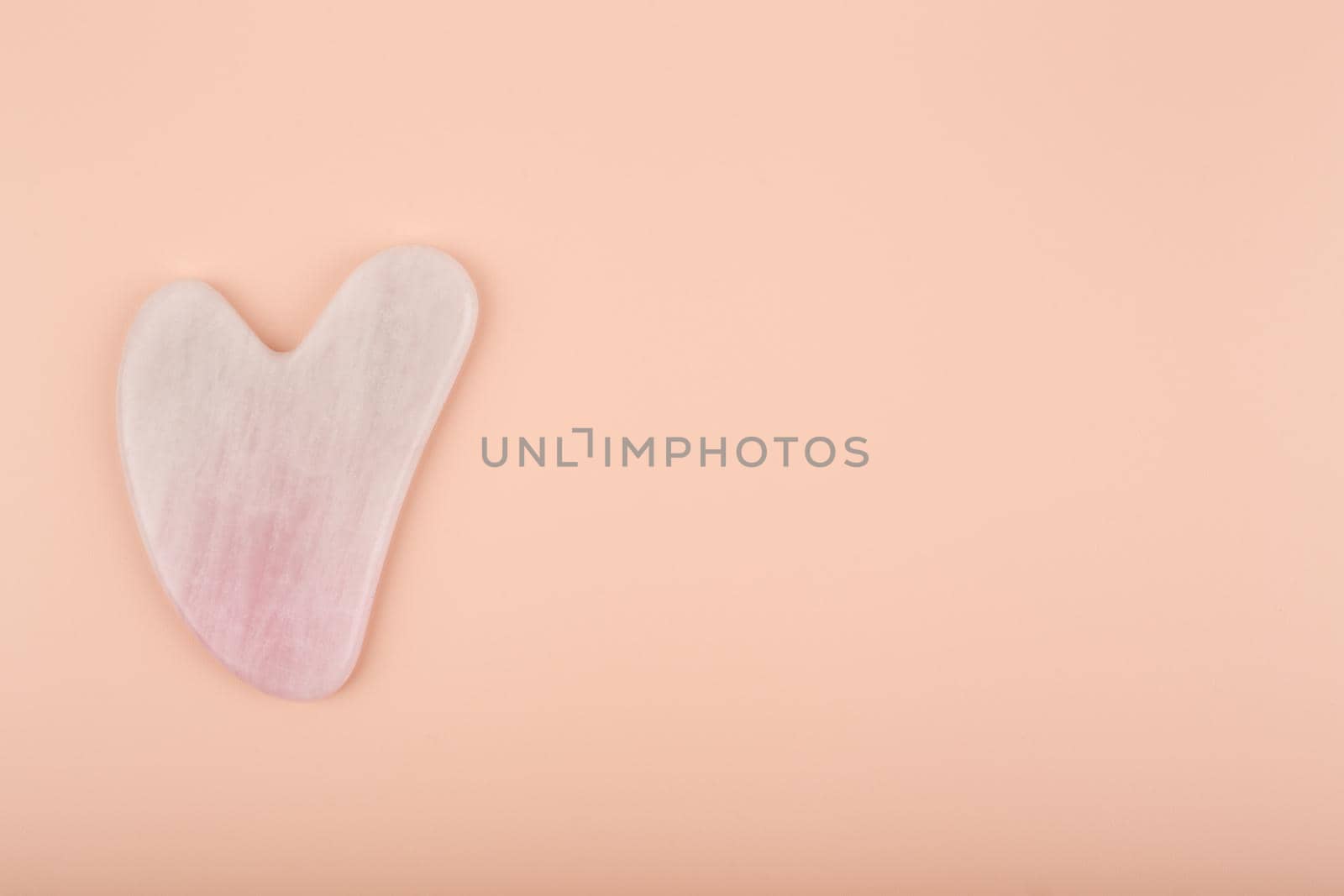 Pink heart shaped guasha stone made of quartz crystal on bright beige background by Senorina_Irina