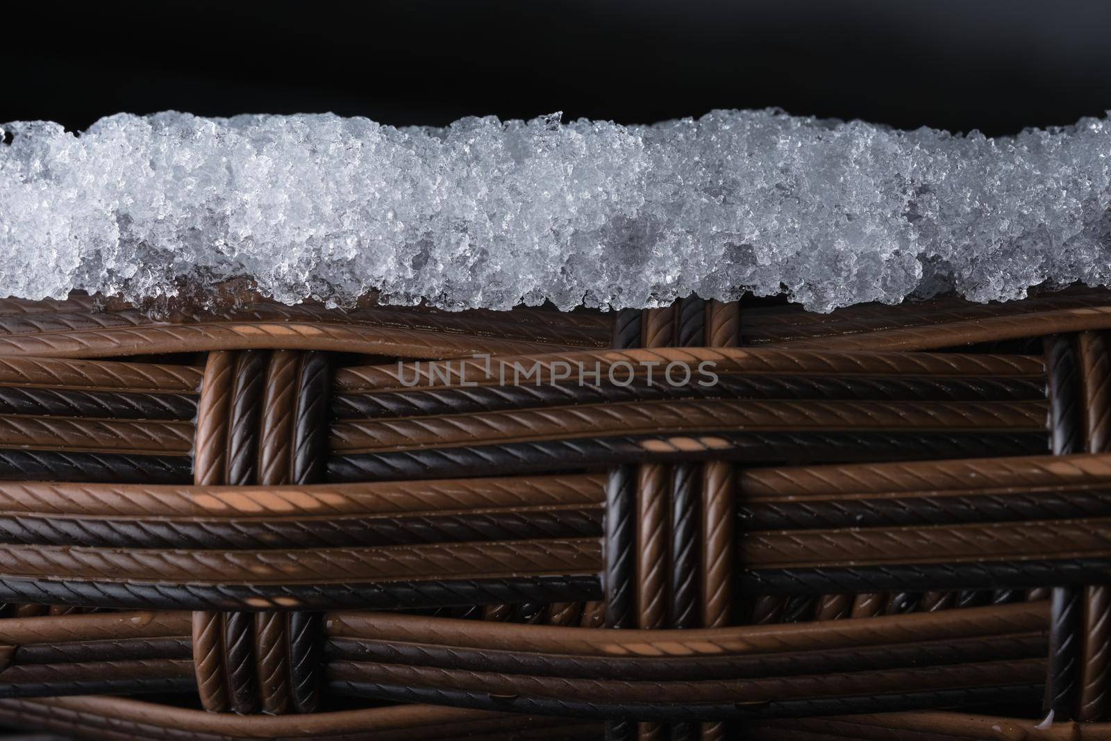 Layer of ice sits on top of textured plastic garden furniture. Copy space over black backgruond, full frame composition. Rope like macro appearance